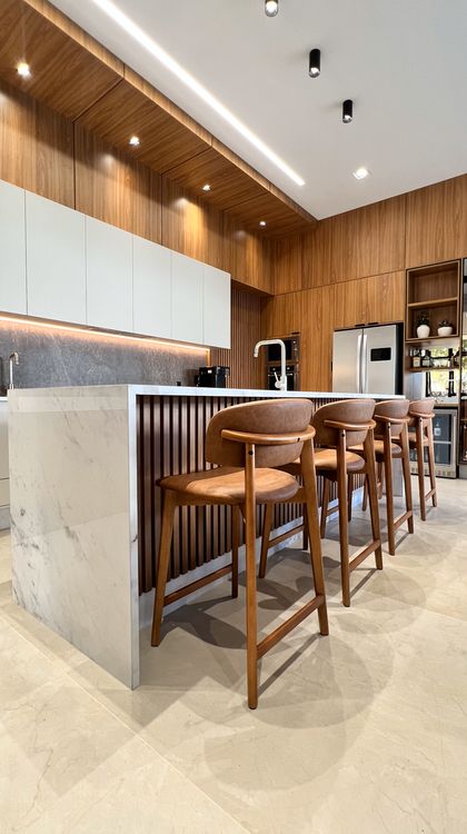 Cocina moderna con isla, taburetes de cuero y revestimiento madera natural — proyecto Residência H&N, por Gaby Boing Arquiteta, en Alta Floresta