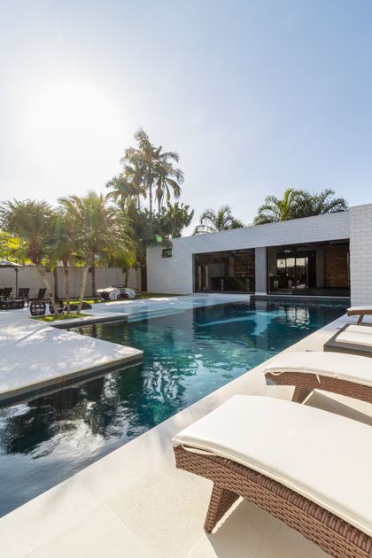 Pileta moderna con deck, sillones y palmeras en exterior residencial — proyecto Mansão de Gabigol, por Carlos Pardal, en Guarujá