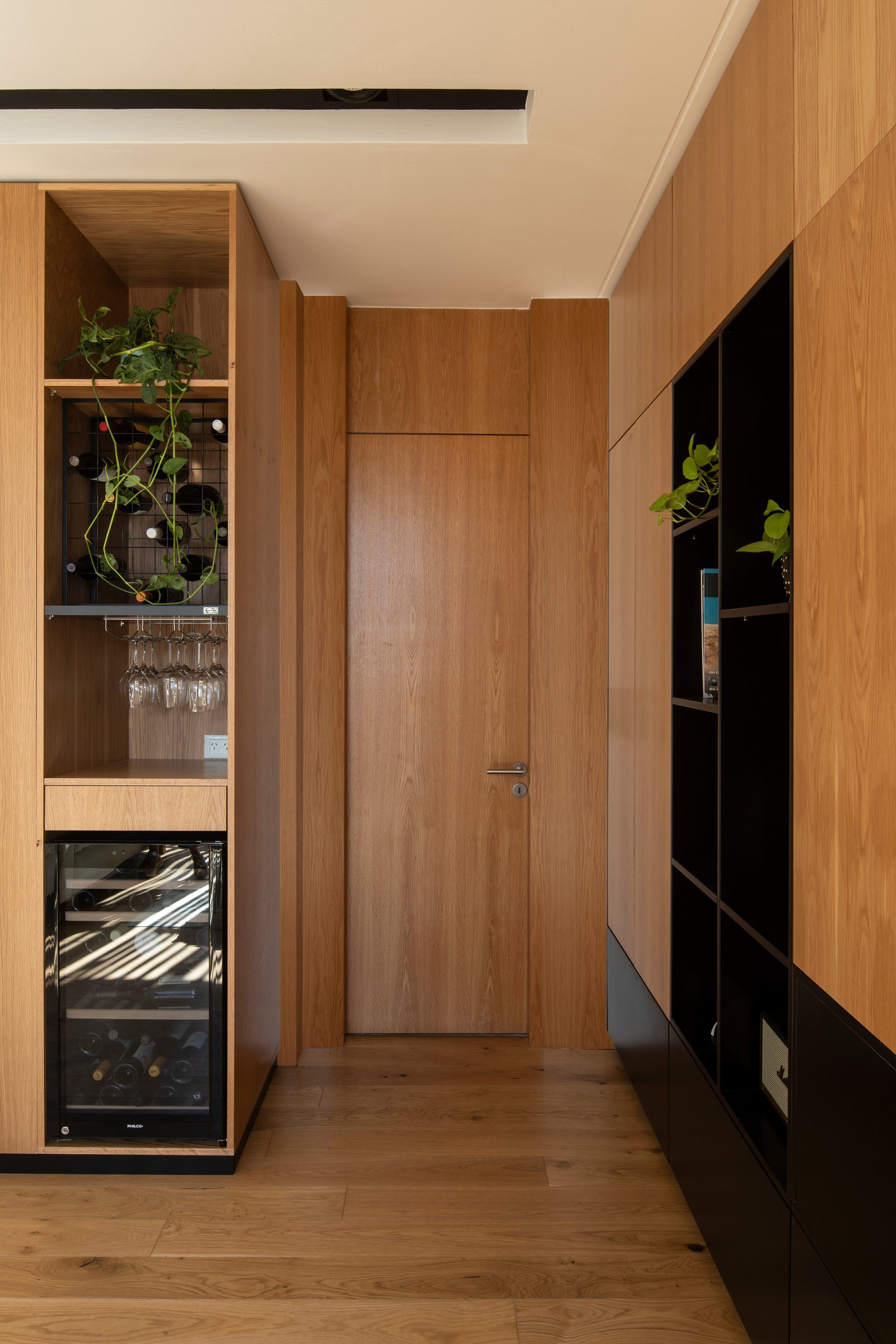 Corredor moderno com painéis de madeira e prateleiras pretas — projeto Casa MECHA, por Grupo CRBN, em B1712 Castelar