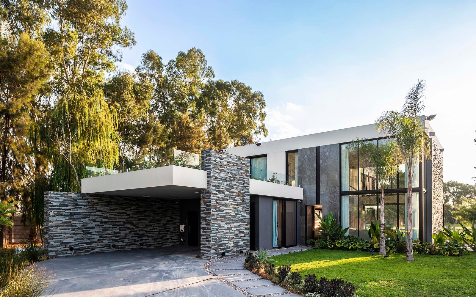 Fachada moderna con piedra natural y ventanales de piso a techo — proyecto CASA T199, por A'PRIMA - Arquitectura Sustentable, en Los Robles 5901