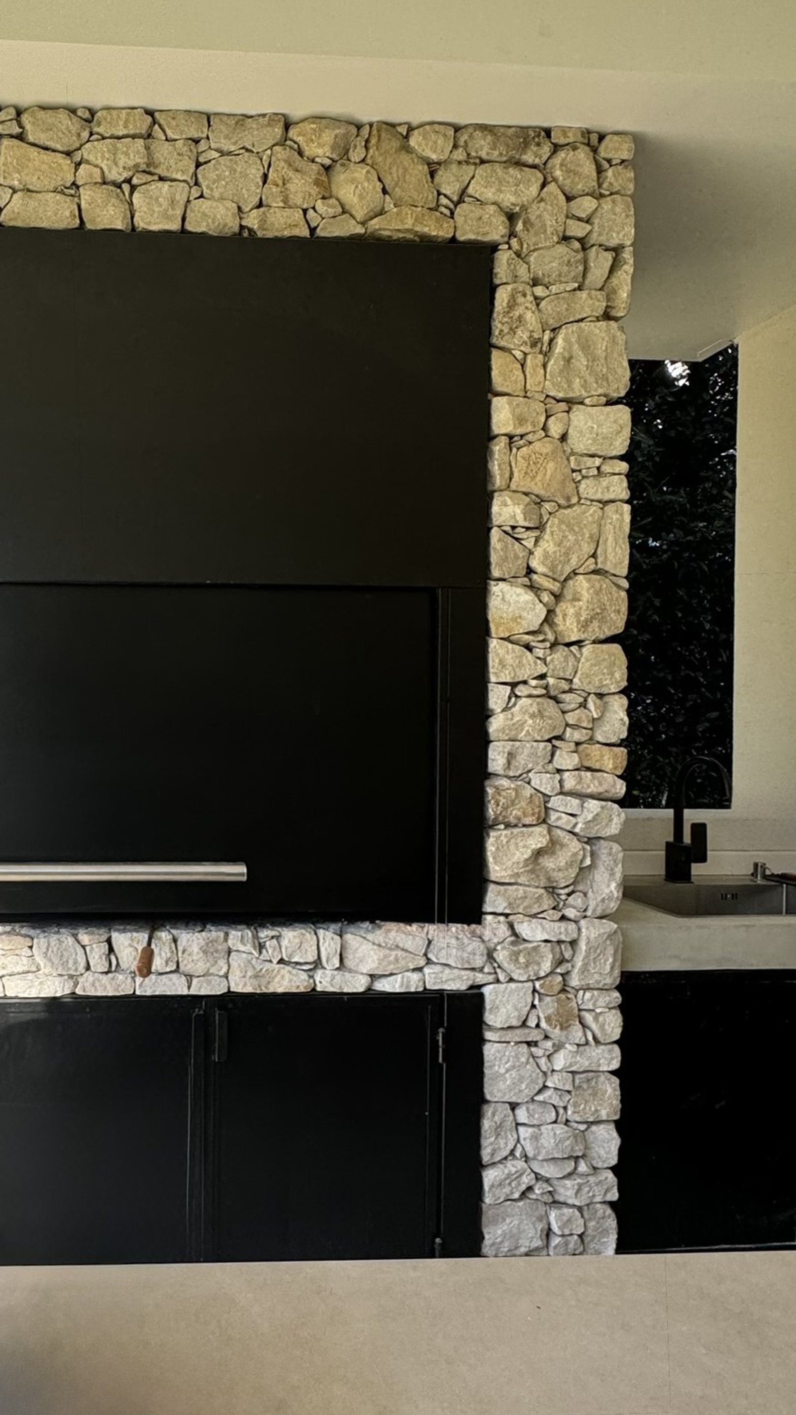 área de quincho moderna con revestimiento de piedra y parrilla negra — proyecto Casa CC, por Hermann Arquitectos, en Los Castores