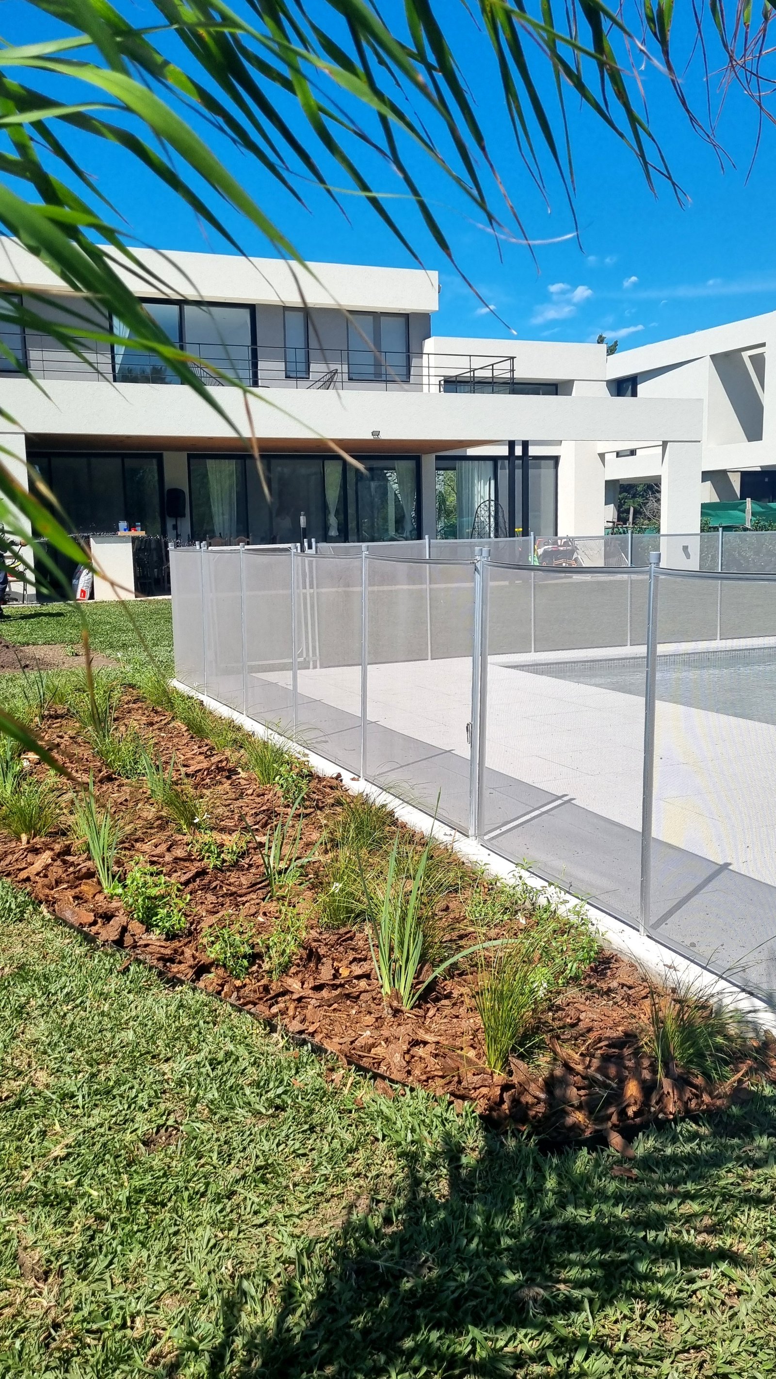 Casa moderna con piscina, césped y cerco de malla — proyecto Ayres del Pilar - La Cañada, por Marcela García Brünner Paisajista, en INF44024 - Colectora Este