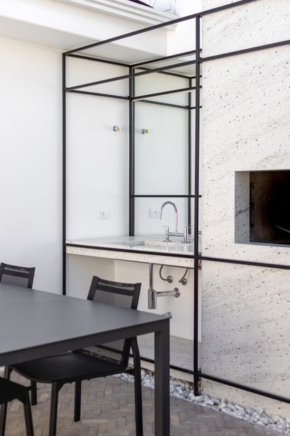 Quincho moderno con parrilla integrada, mesada de piedra clara y mesa de metal — proyecto Residencial, por  Rodolfo Fontana