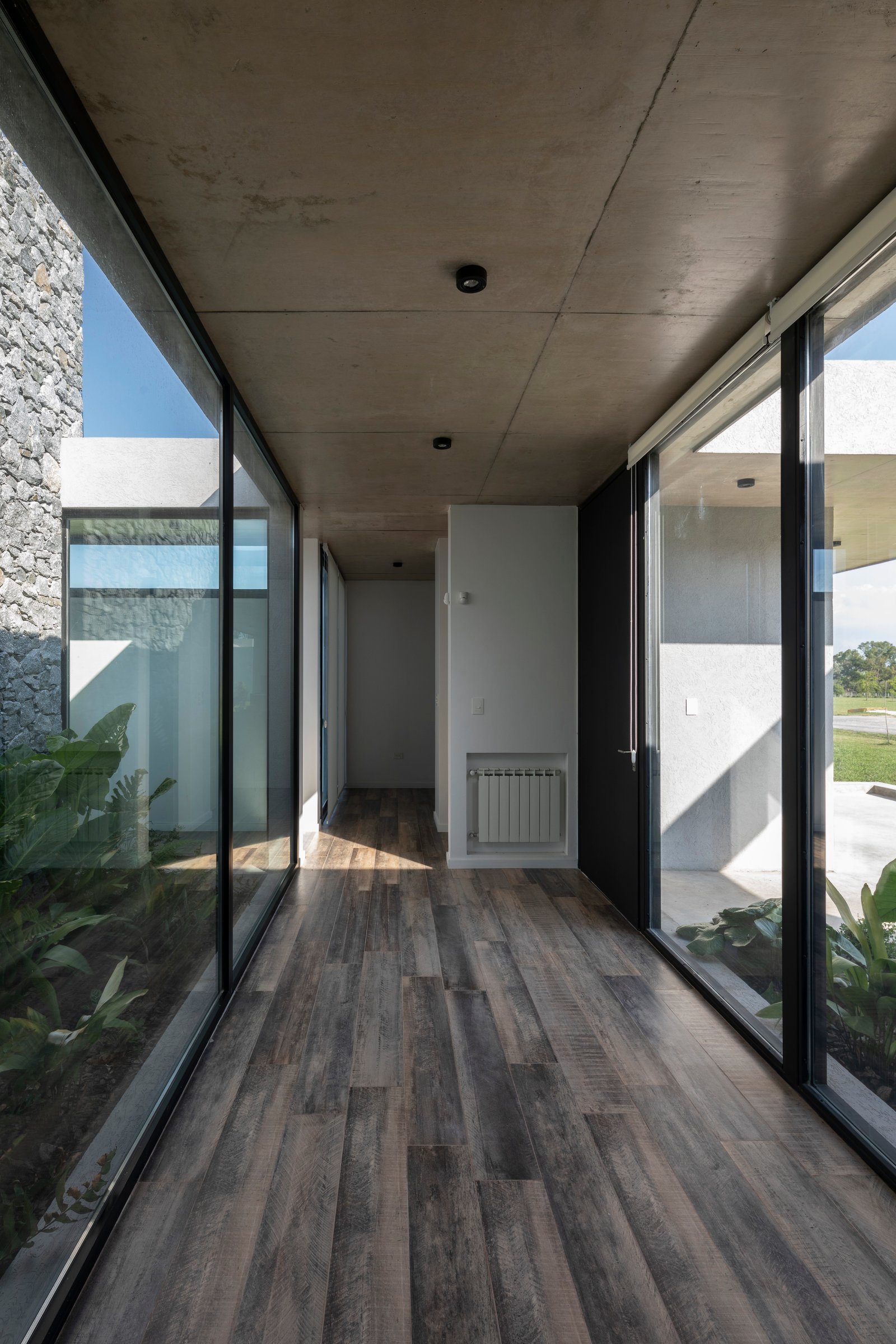 Pasillo moderno con techo y muros de hormigón visto y suelo de madera — proyecto Casa Cruz , por Grupo CRBN, en B2812 Exaltación de la Cruz