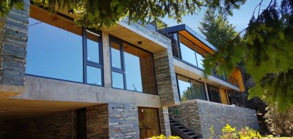Fachada moderna de montaña con grandes ventanales y revestimiento de piedra — proyecto Casa Península San Pedro, por Servente Larrazabal Arq, en Bariloche