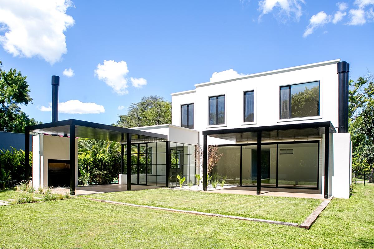 Casa moderna branca com pérgola preta, jardim e churrasqueira externa — projeto Bosque Chico, por Estudio Arq. María Sioli, em Garin