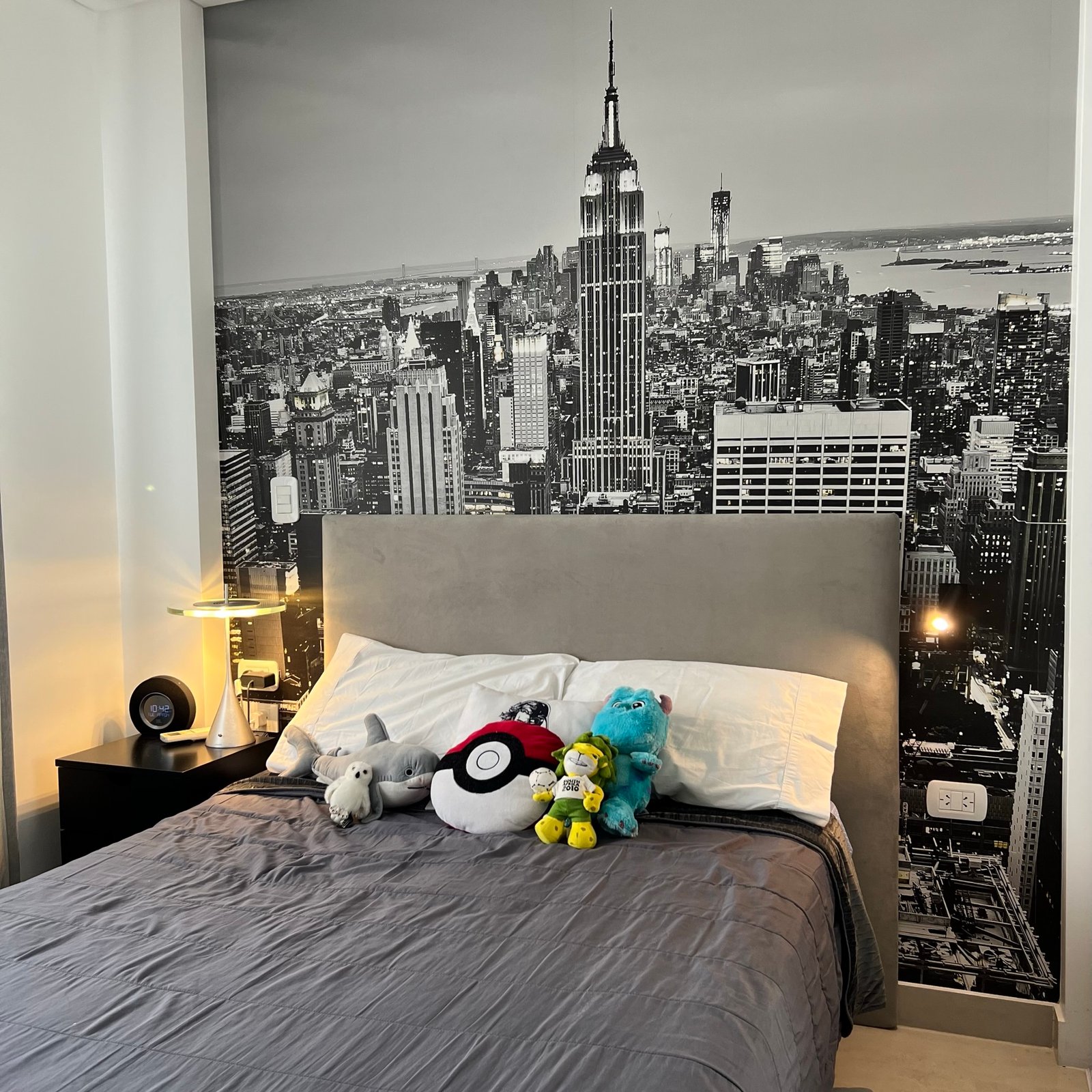 Dormitorio moderno con mural de ciudad, cama gris y luz cálida — proyecto Basualdo II, por MDBK Arquitectura, en Liniers