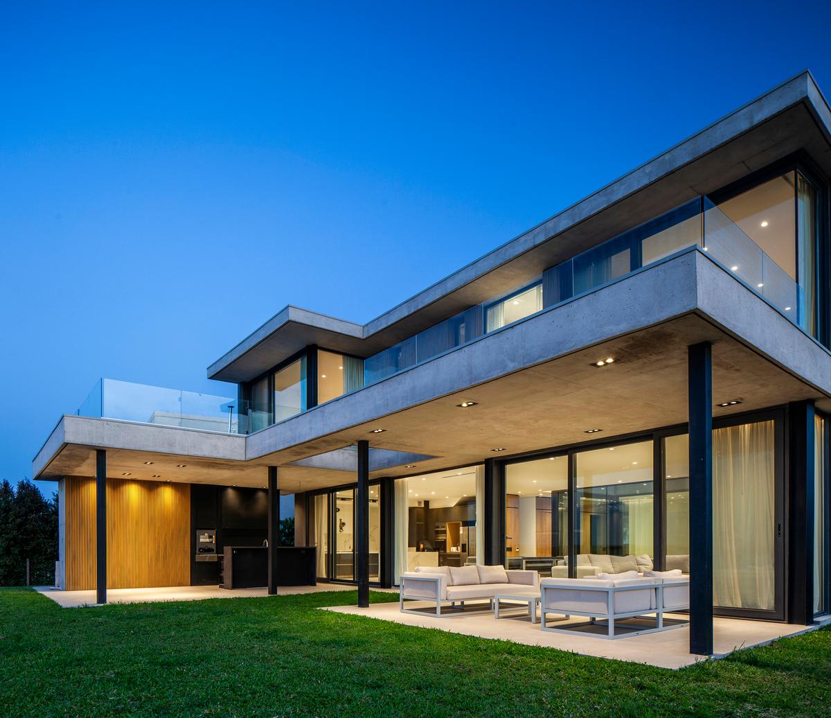 Fachada de casa moderna em concreto aparente com amplas janelas — projeto CASA MUELLES 239, por ABAD GADANO, em Belén de Escobar