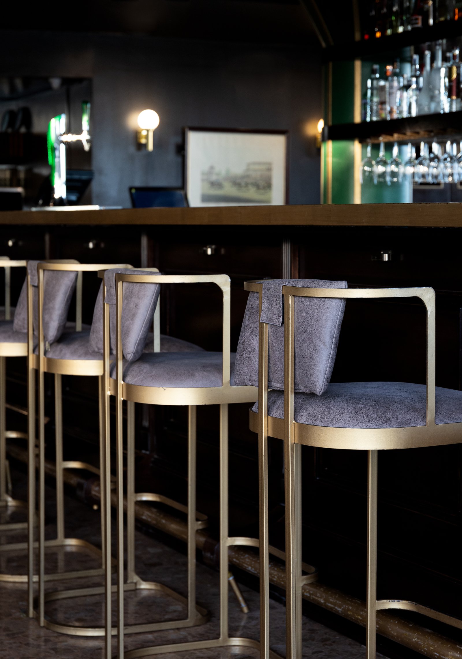 Banquitos de bar dorados y grises frente a una barra oscura — proyecto PRESIDENTE BAR HIPODROMO, por AB ARQUITECTURA, en San Isidro