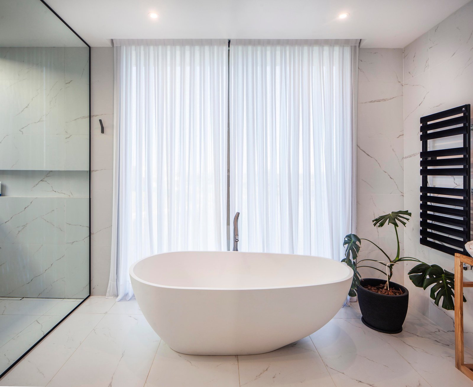 Baño moderno con bañera exenta ovalada blanca y paredes de mármol — proyecto CASA C313, por A'PRIMA - Arquitectura Sustentable, en Provincia de Buenos Aires