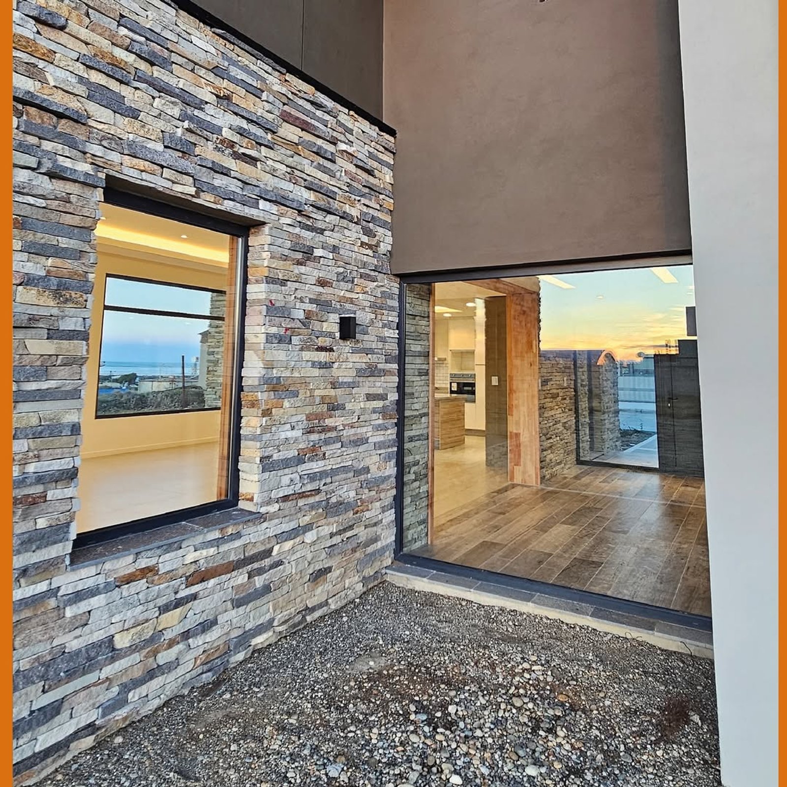 Fachada moderna con piedra apilada y grandes ventanales al mar — proyecto Casa Kren, por MUCHTEK, en Río Grande