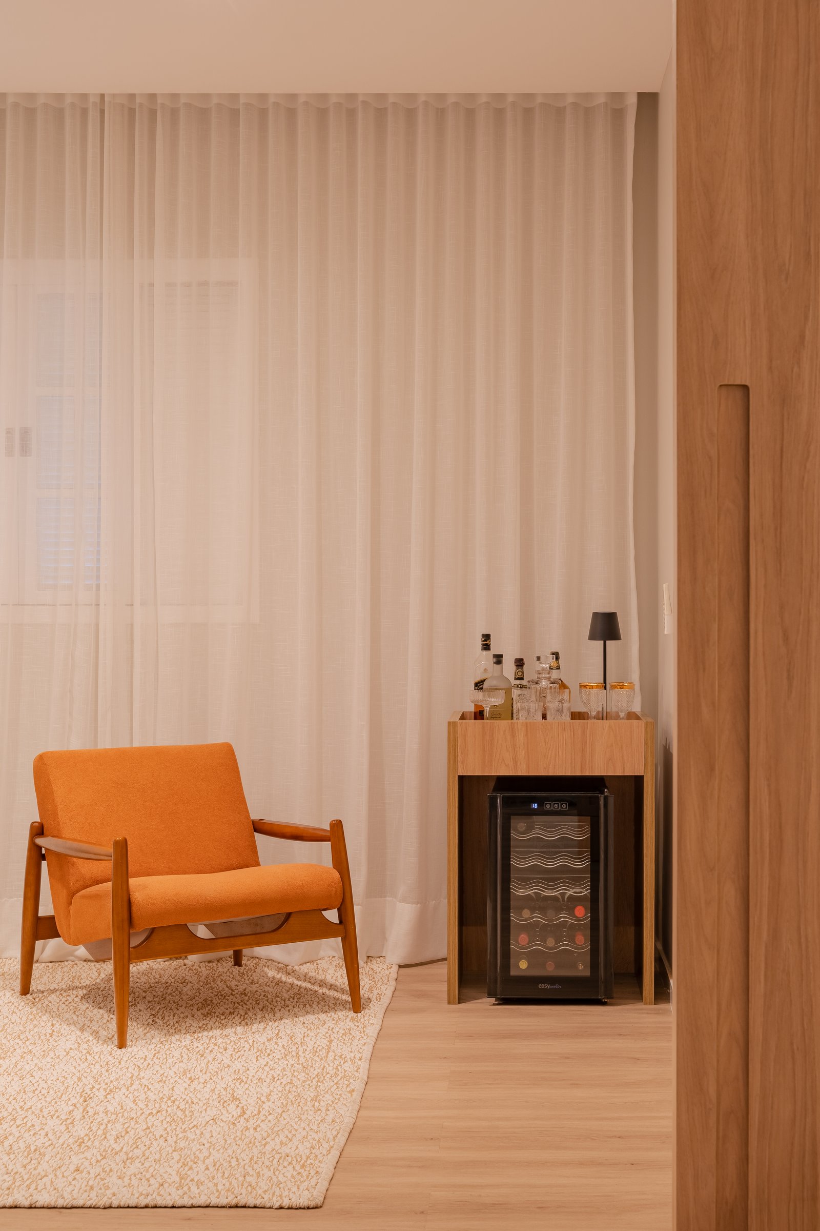 Living con sillón naranja, cortinas blancas y cava de vinos — proyecto Projeto DL, por Felipe Rohen, en Niterói