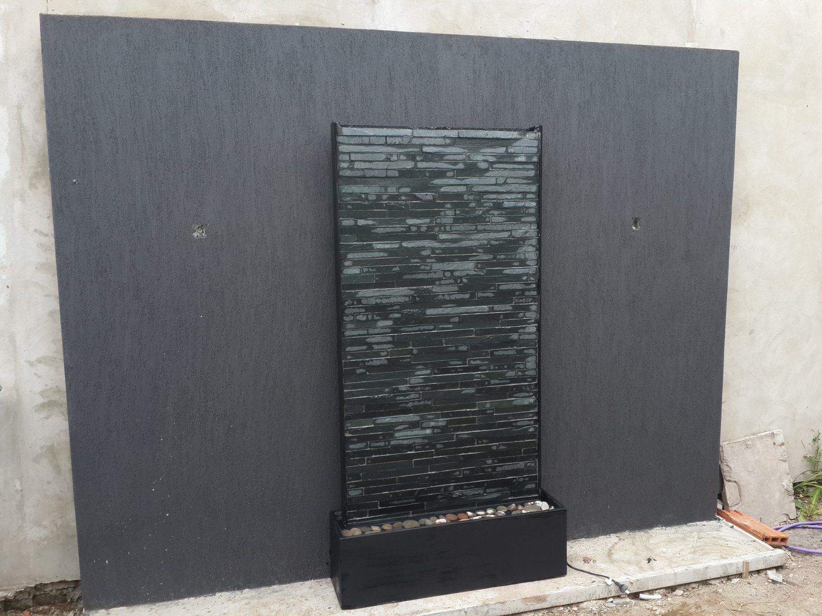 Cascata moderna em pedra contra parede escura — projeto Muro Agua Piedra Negra, por FUENTES Y MUROS .COM.AR, em Ruta Panamericana Km 32