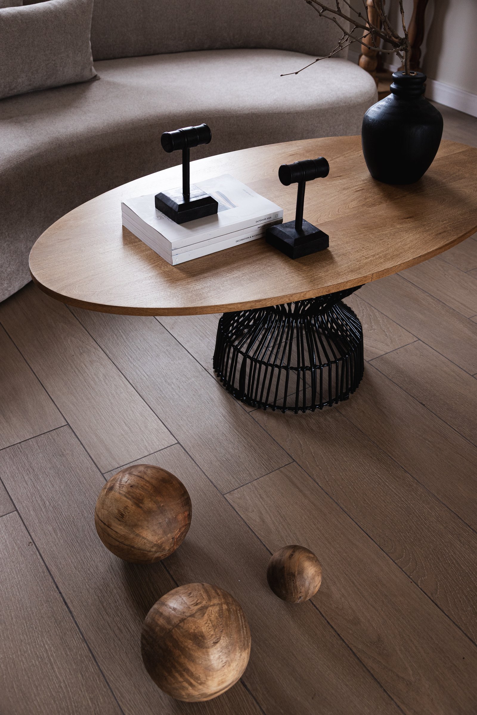 Sofá curvo beige junto a mesa de centro oval de madera y base de canasta negra — proyecto Styling para Grumsdelg - CBA, por El Marques deco y ambientaciones, en Córdoba