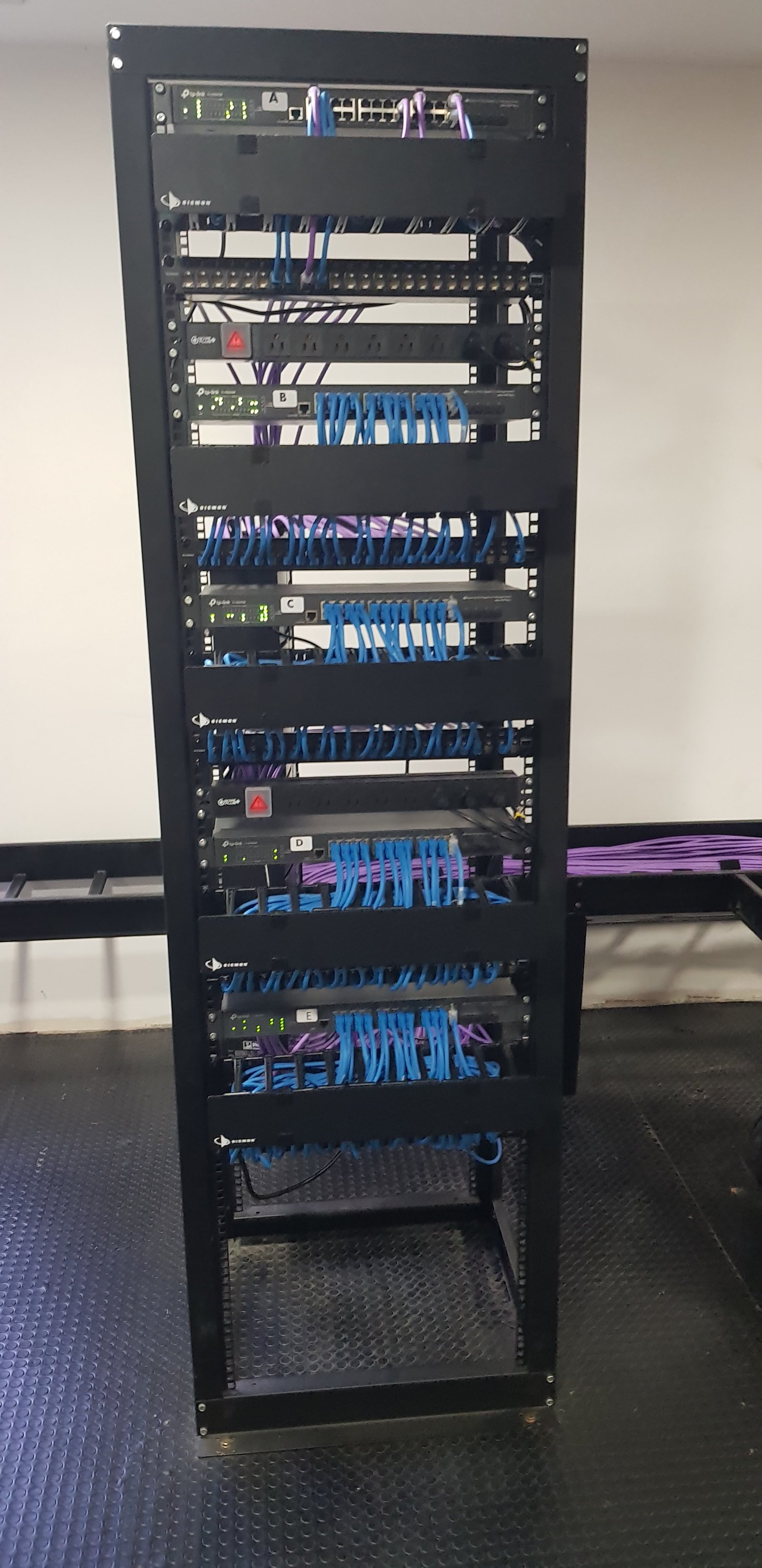 rack de red metálico negro con cables azules y púrpuras — proyecto Montajes eléctricos en oficinas Comerciales , por Mantenimientos Comerciales Leon , en Buenos Aires
