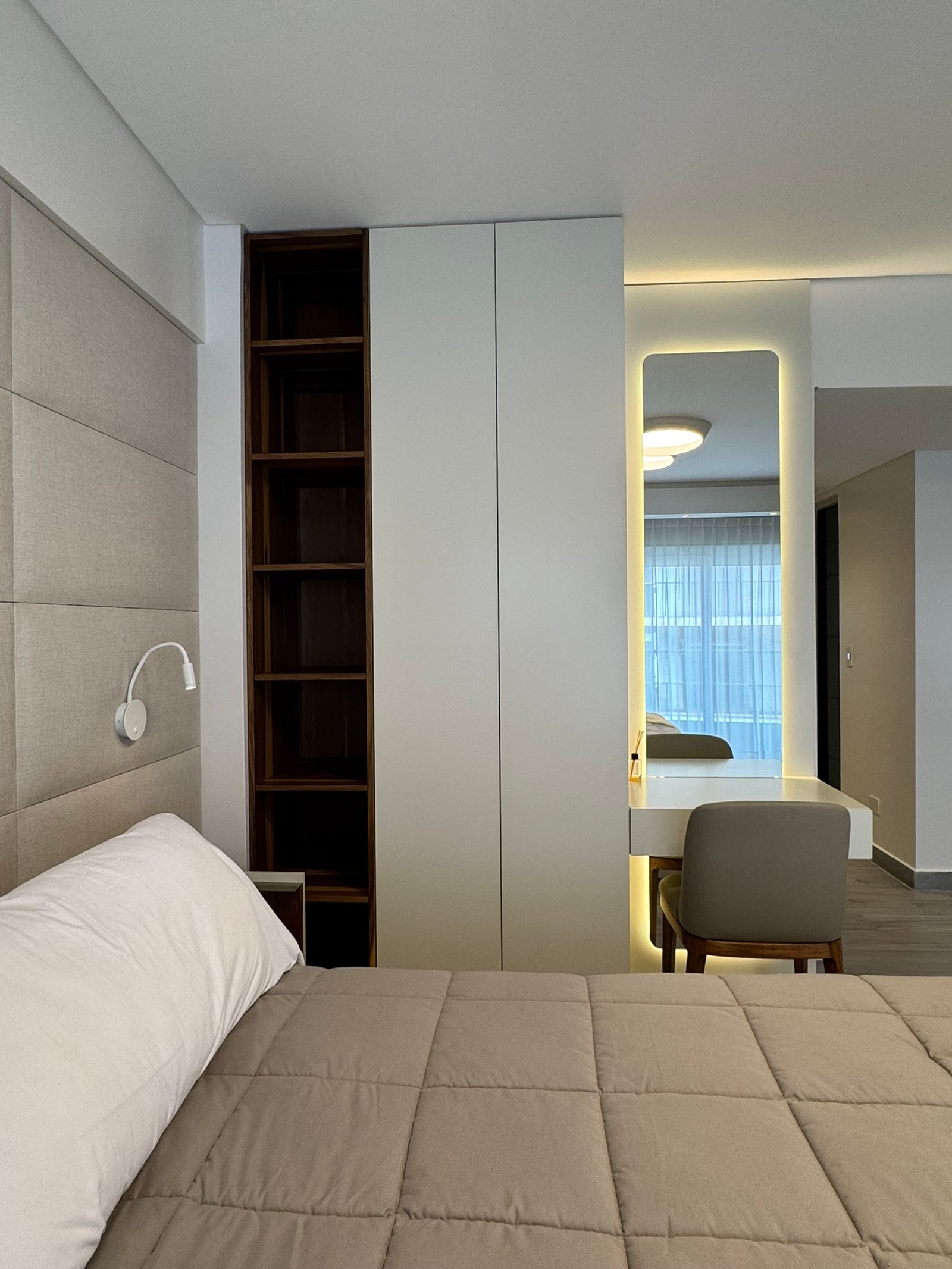 Dormitorio moderno con cama beige, espejo retroiluminado y estantería oscura — proyecto Cerviño, por MDBK Arquitectura, en Palermo