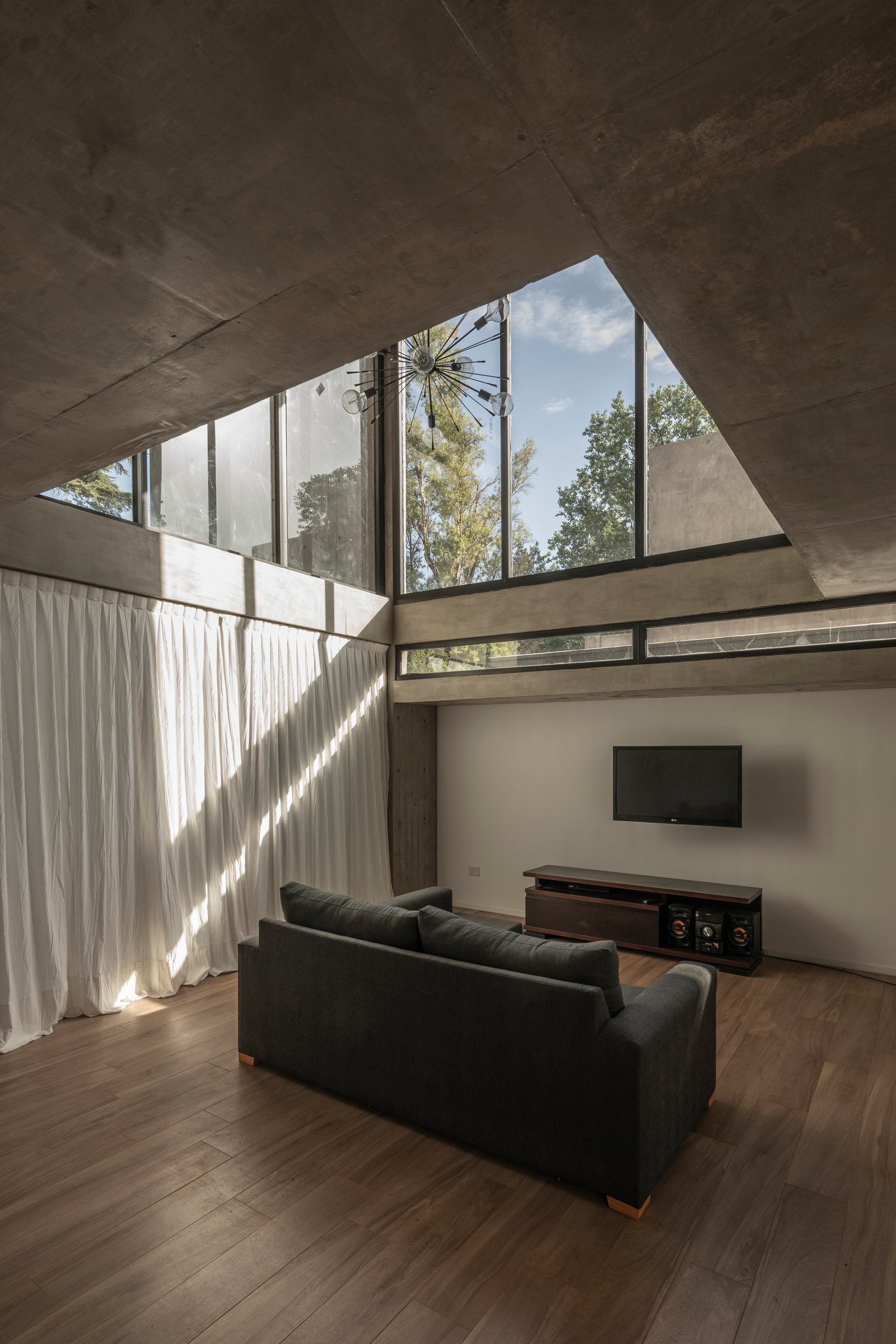 Living moderno brutalista con hormigón expuesto y gran ventanal — proyecto Casa Emilia, por Grupo CRBN, en Parque Leloir