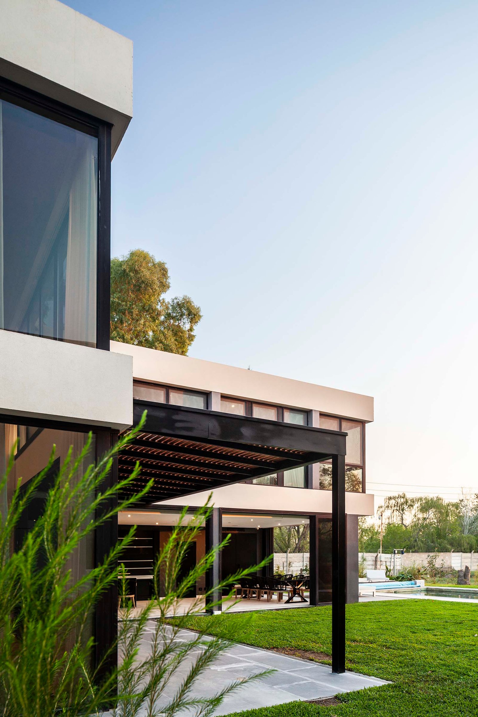 Fachada moderna con vegetación prominente y pérgola — proyecto CASA T199, por A'PRIMA - Arquitectura Sustentable, en Los Robles 5901