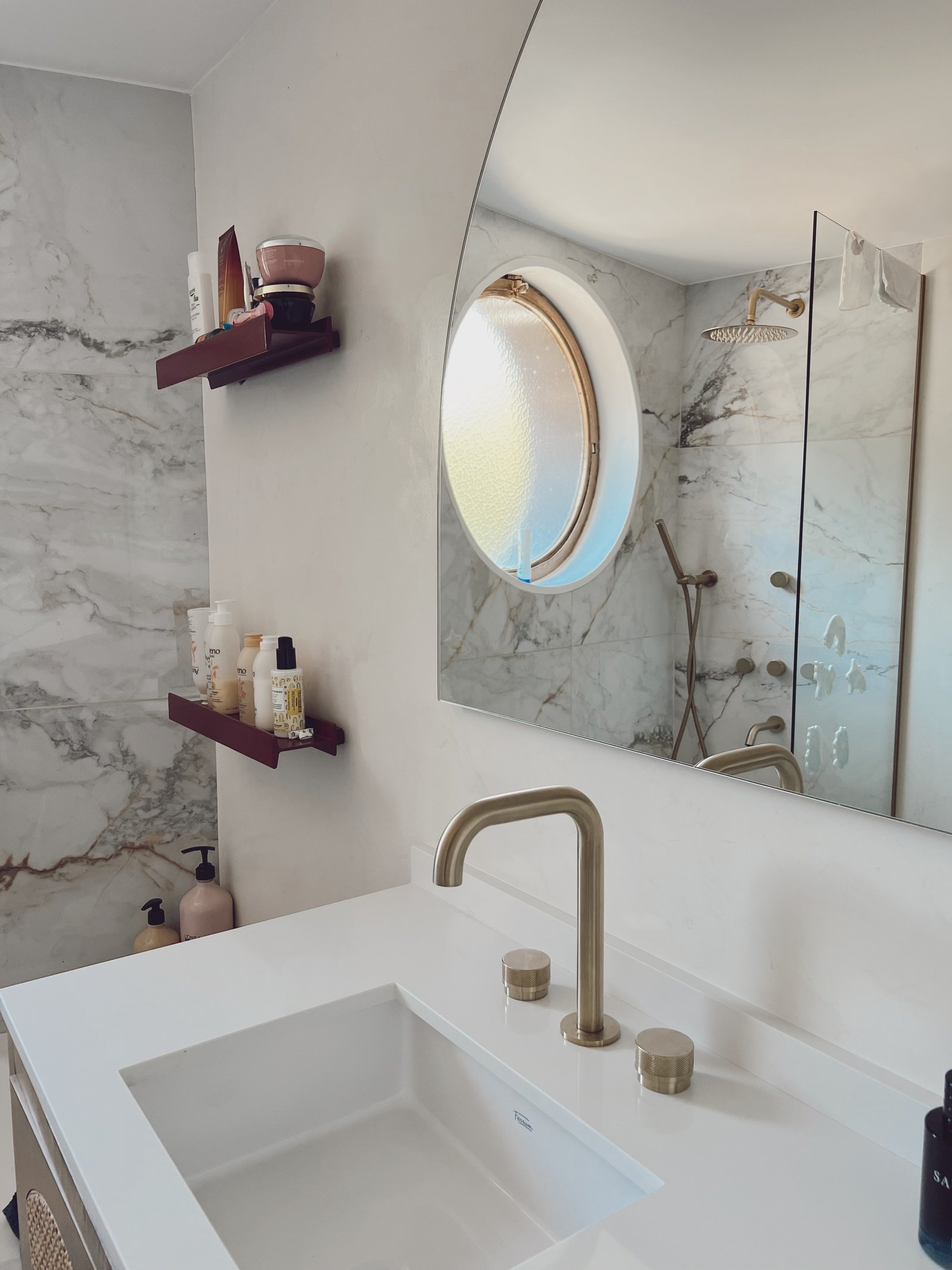 Baño moderno con espejo ovalado, grifería dorada y paredes de mármol — proyecto Figueroa Alcorta 2, por Equipe, en Buenos Aires