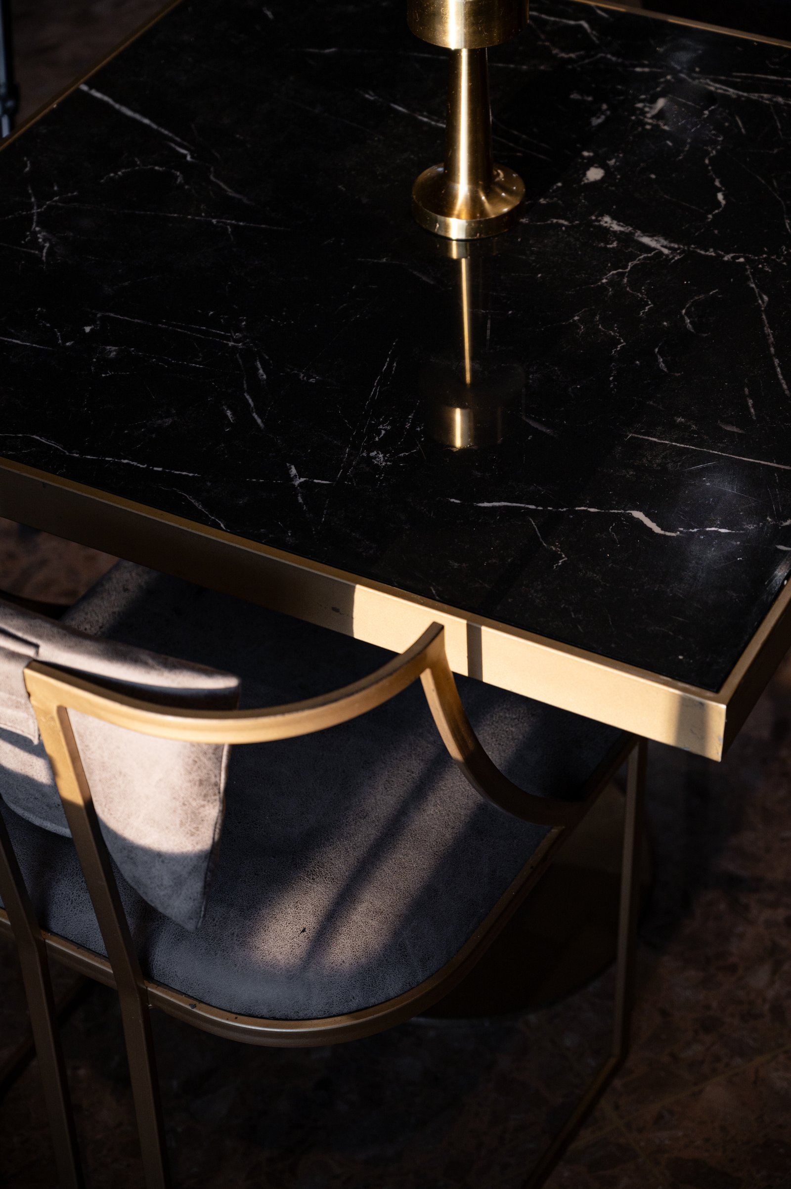 Mesa de mármol negro con sillas tapizadas en gris y detalles en bronce — proyecto PRESIDENTE BAR HIPODROMO, por AB ARQUITECTURA, en San Isidro