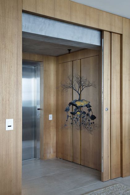 Pasillo moderno con ascensor y puerta de madera, instalación artística árbol — proyecto PL House, por Studio Ro-ca