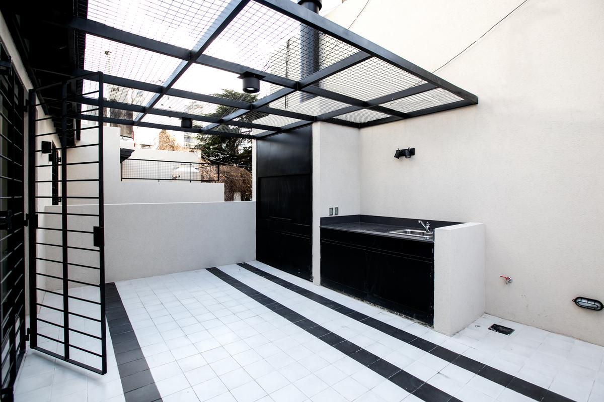 Área de churrasco moderna com grelha e pia, teto de pergolado metálico preto — projeto PH Bustamante, por Escalante Vela Arquitectos, em CABA