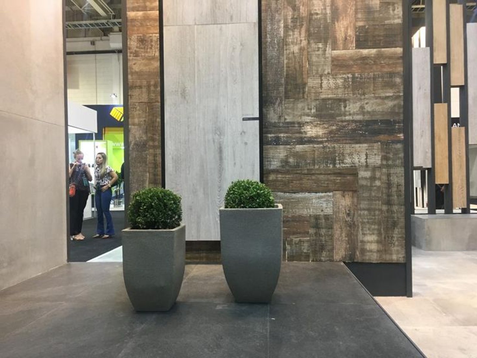 corredor com painéis de madeira texturizada e vasos cinzas — projeto Expo Revestir 2019, por Vite Porcellanato, em São Paulo