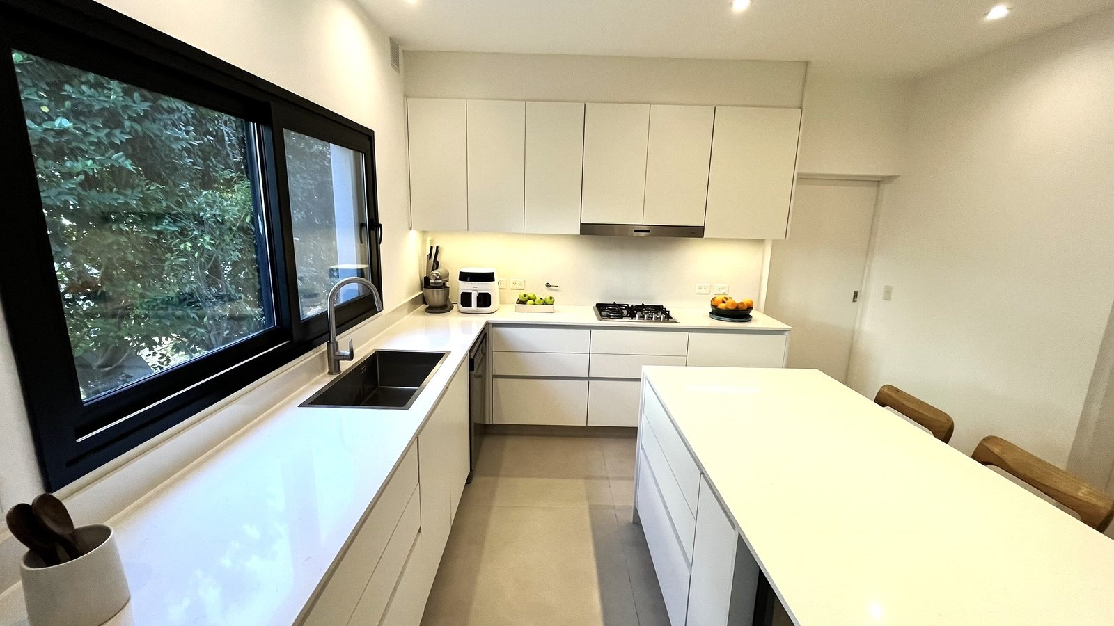 Cocina moderna minimalista con isla blanca y grandes ventanales — proyecto Casa Vir (Barrio El Lucero, Buenos Aires) German Salas arquitectura , por German Salas arquitectura - San