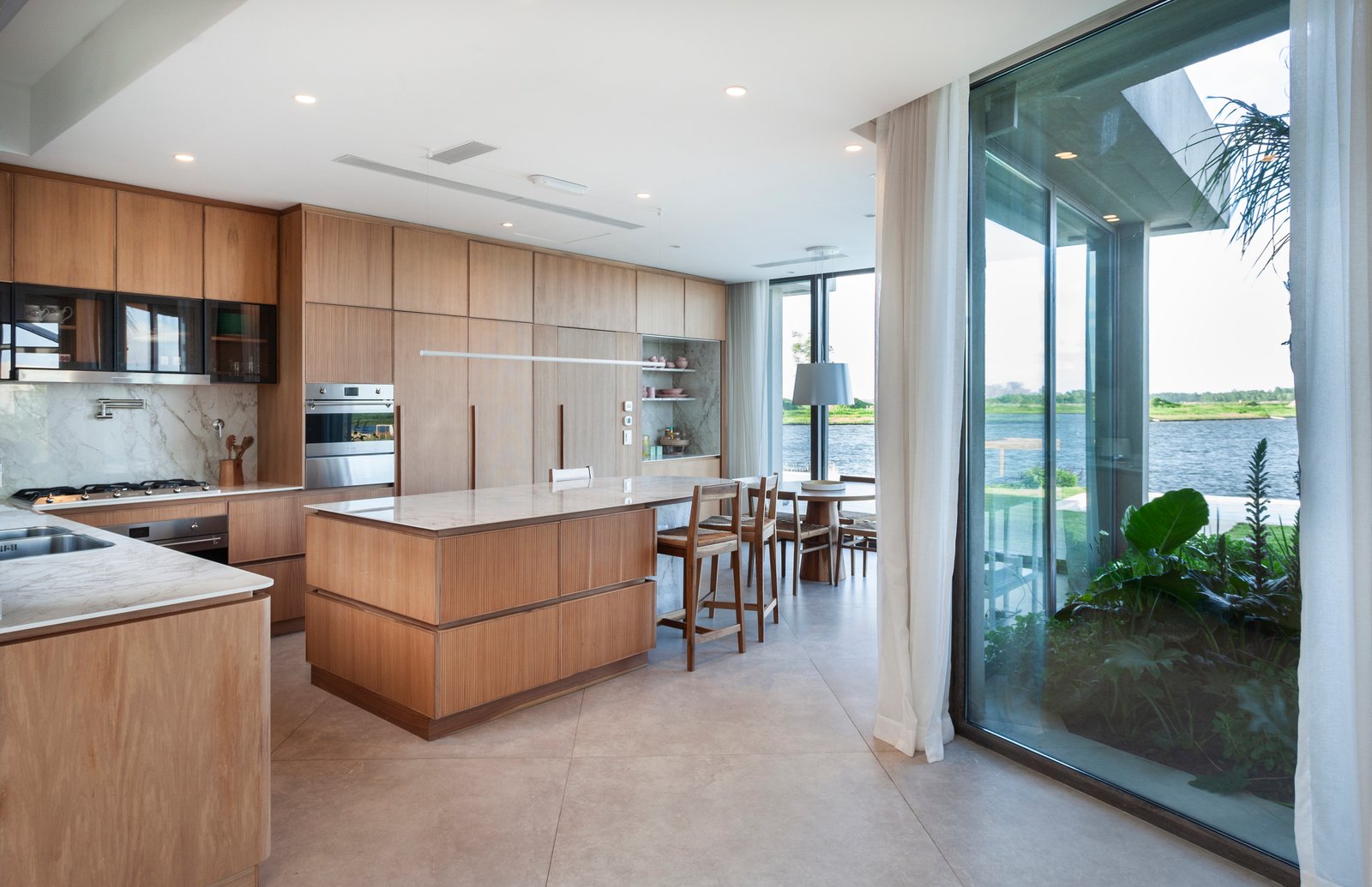 Cocina moderna con isla y ventanales al agua y jardín — proyecto CASA M40, por A'PRIMA - Arquitectura Sustentable, en Unnamed Road