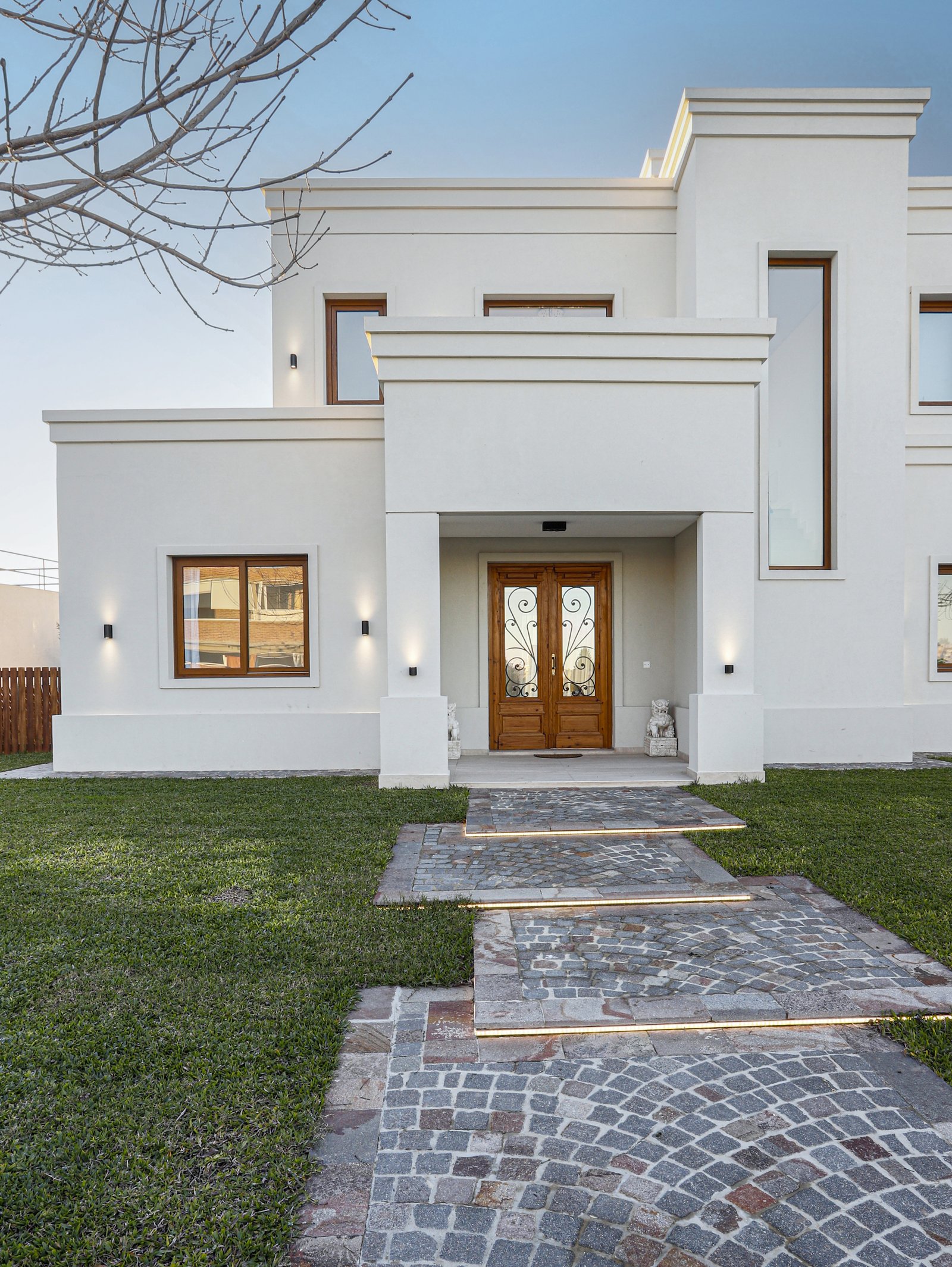 Fachada moderna blanca con camino de piedra iluminado — proyecto Casa SS182, por EZ architects, en M3CV+6H