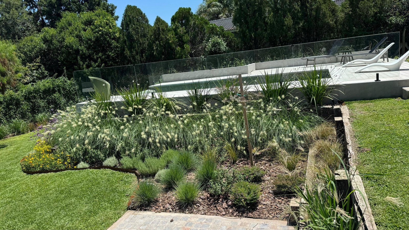 Área de piscina moderna con vegetación exuberante y muebles blancos — proyecto La Paloma :: Villa Allende - Córdoba :: Paisajismo Residencial :: STIPA Arte Nat, por STIPA Arte Natu