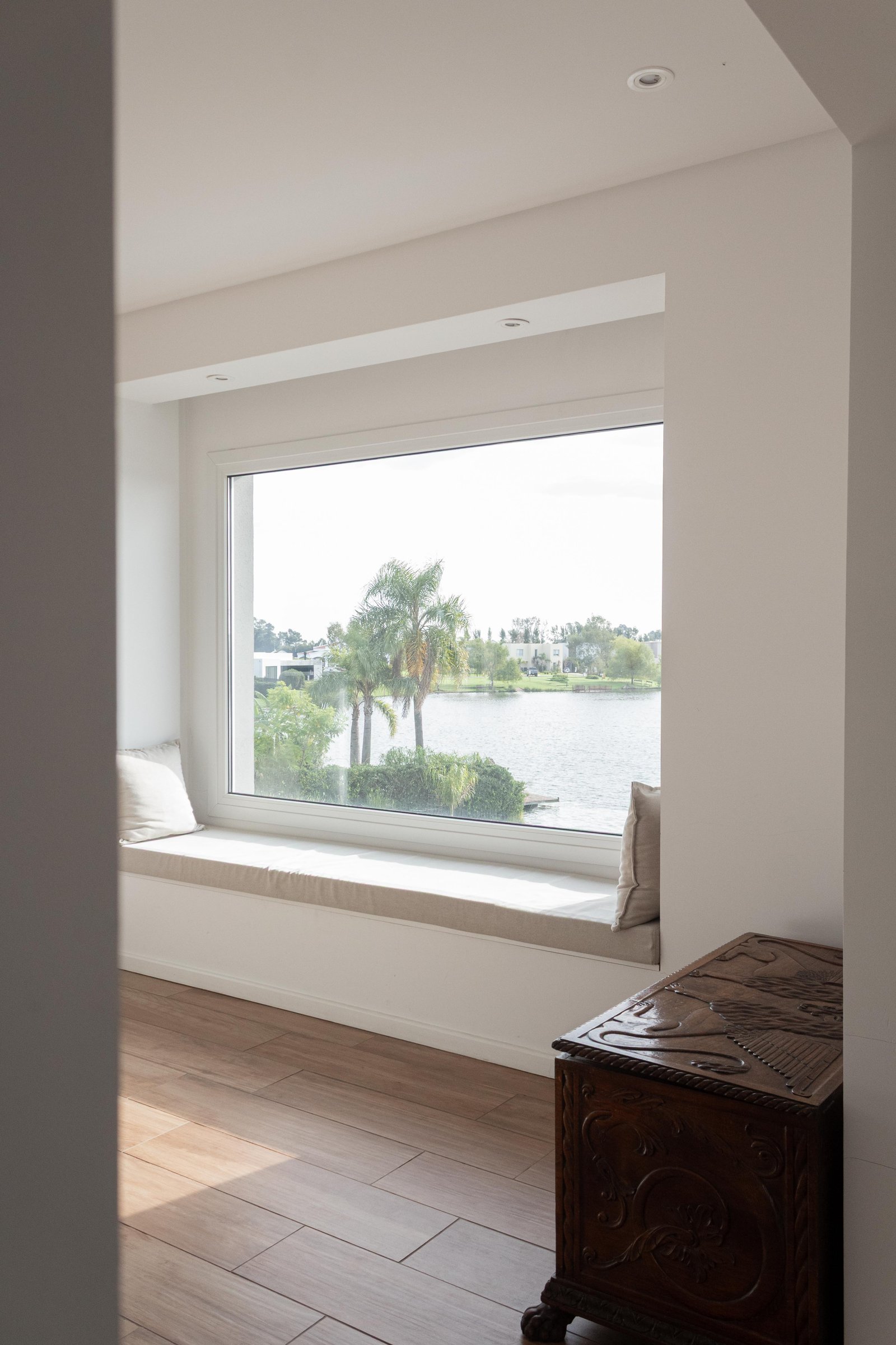 Sala de estar moderna con ventana panorámica a un lago y cofre de madera tallada — proyecto San Rafael, por Catalina Fitero Fotografìa, en Blvd. de Todos los Santos 3500