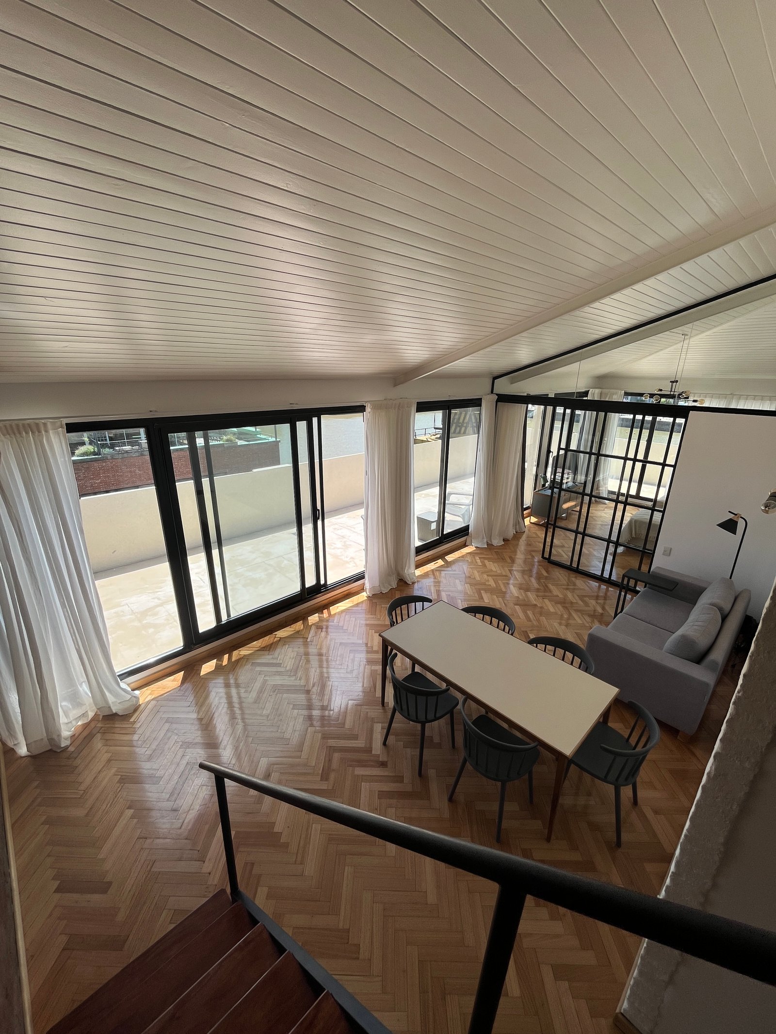 Comedor moderno con piso de madera, grandes ventanales y sillón gris — proyecto Departamento Puerto Madero, por Arcucci Arquitectura, en Puerto Madero
