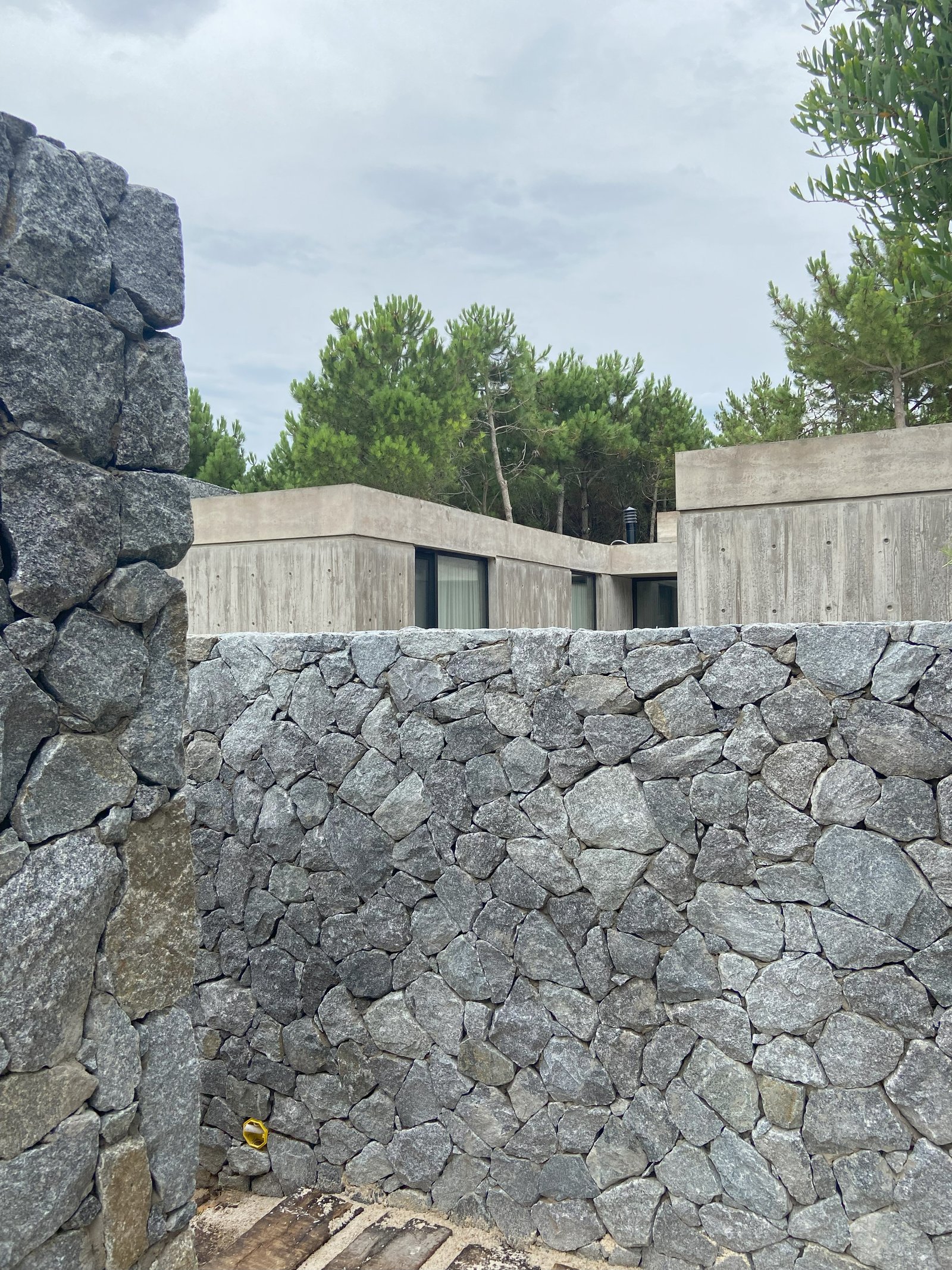 fachada moderna con muros de piedra y hormigón en bosque — proyecto Casa Bunker, por zuloagastudio, en X6VF+67