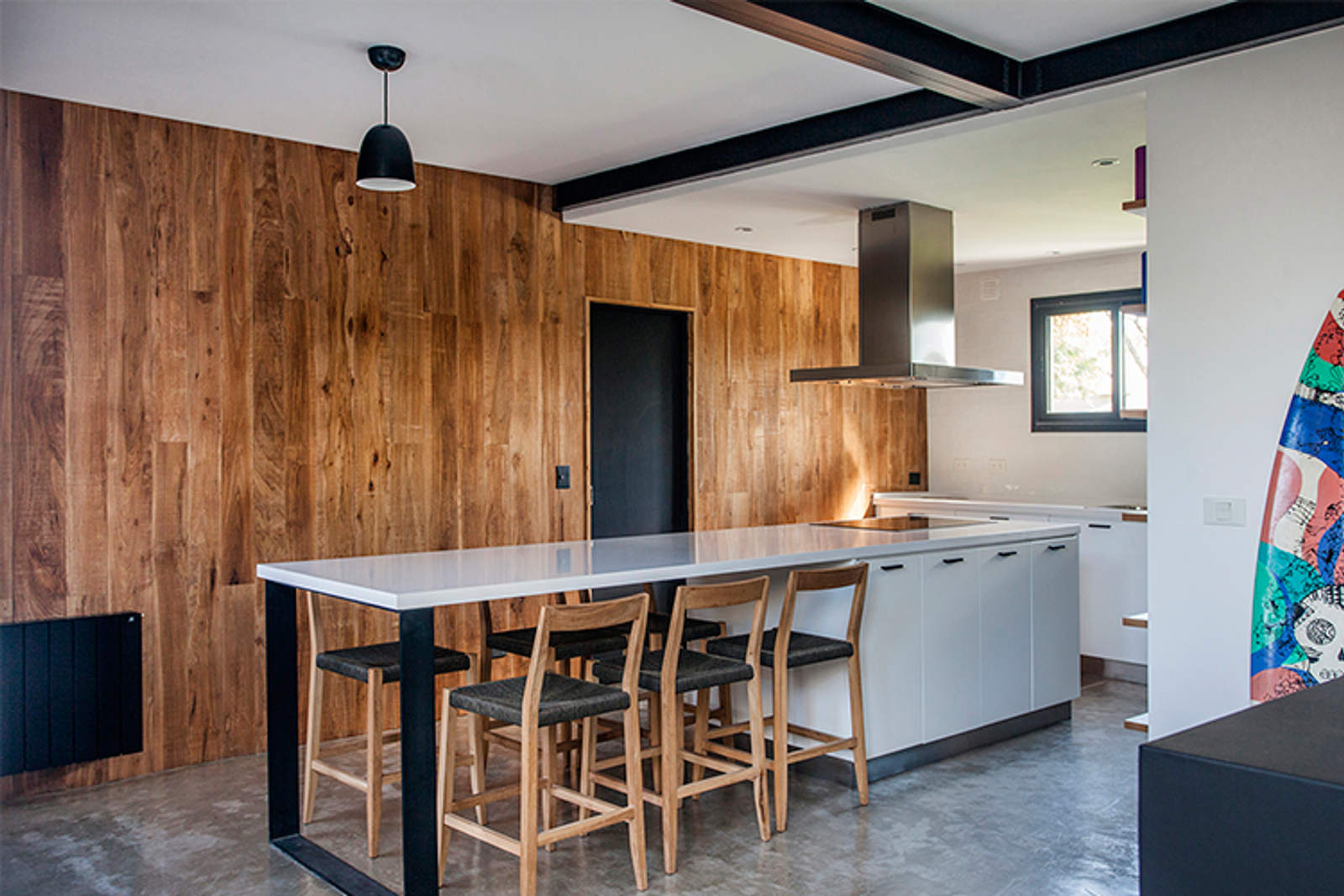 Cozinha moderna com parede de madeira, ilha branca e vigas industriais — projeto Casa coco, por Estudio PK, em B1648 Tigre