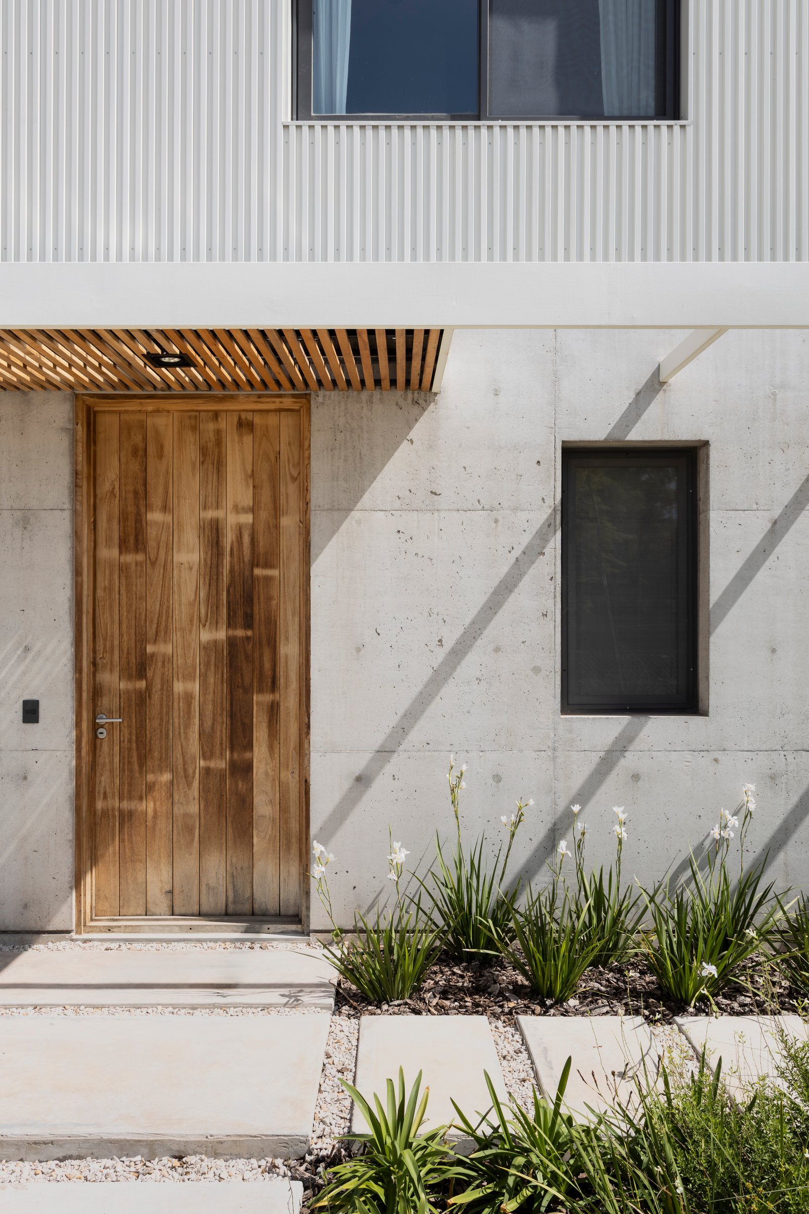 Fachada moderna de hormigón y madera con puerta principal de madera — proyecto CASA CC, por Rastro Estudio, en San Isidro