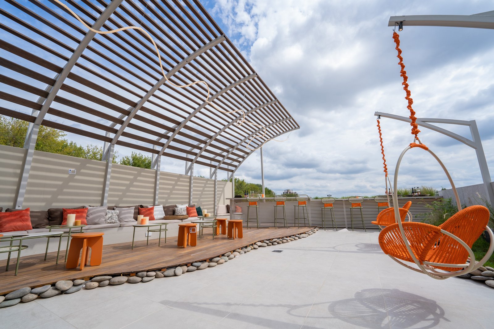 Patio moderno con sillas colgantes naranjas y techo de lamas — proyecto Cementos, por Vite Porcellanato