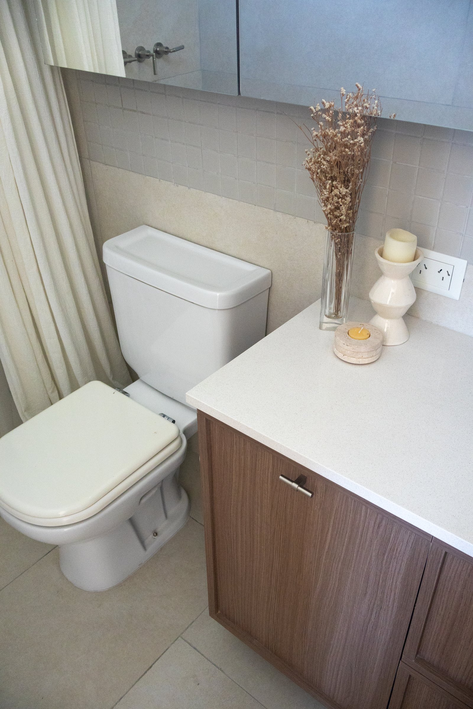 Baño moderno con inodoro blanco, mueble de madera y florero con flores secas — proyecto Cabrera, por Estudio BDM, en Cdad. Autónoma de Buenos Aires