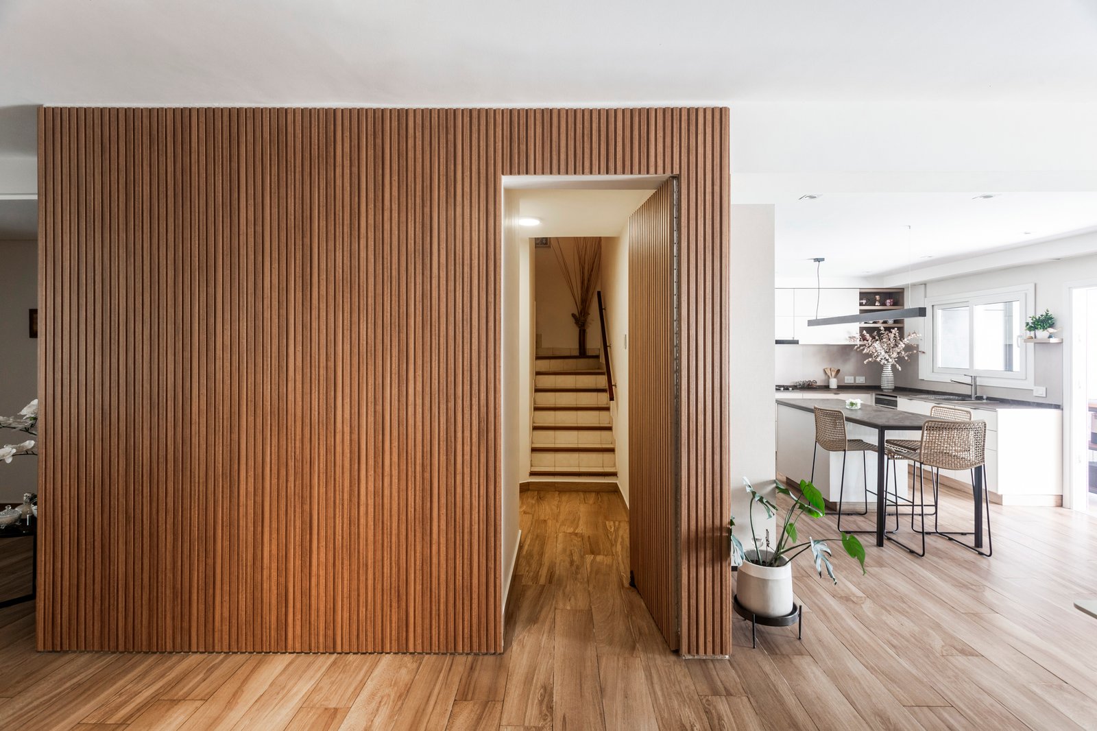 Pared de madera ranurada oculta, escalera flotante, cocina y living — proyecto Casa en Martinez, por JT ARQUITECTURA, en Martínez
