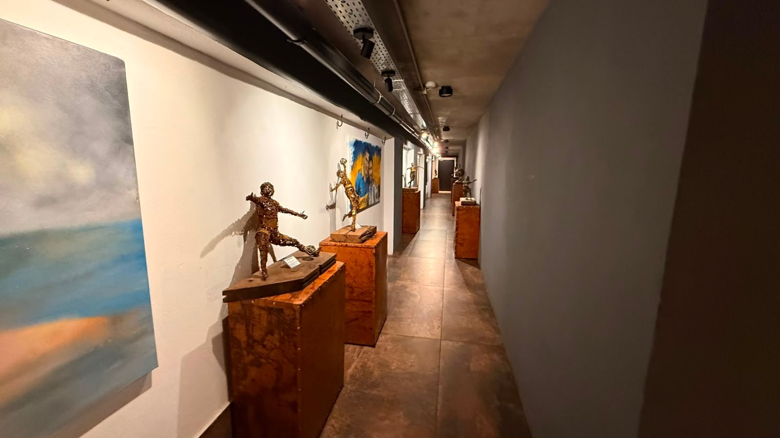 Pasillo de galería de arte moderno con esculturas y cuadros — proyecto UNDICI - Howard Johnson- La Boca, por COMOTTO - SOMMER  - ARQUITECTOS, en Brandsen 927