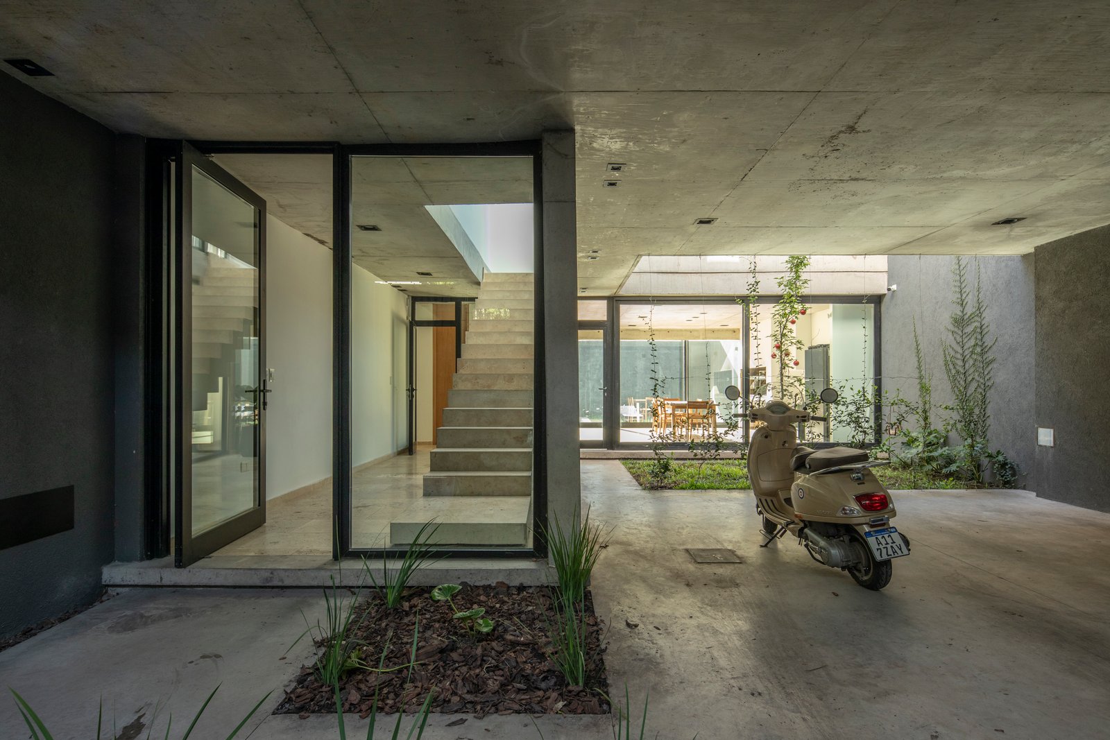 Entrada moderna con hormigón expuesto y scooter estacionado — proyecto Casa MECHA, por Grupo CRBN, en B1712 Castelar