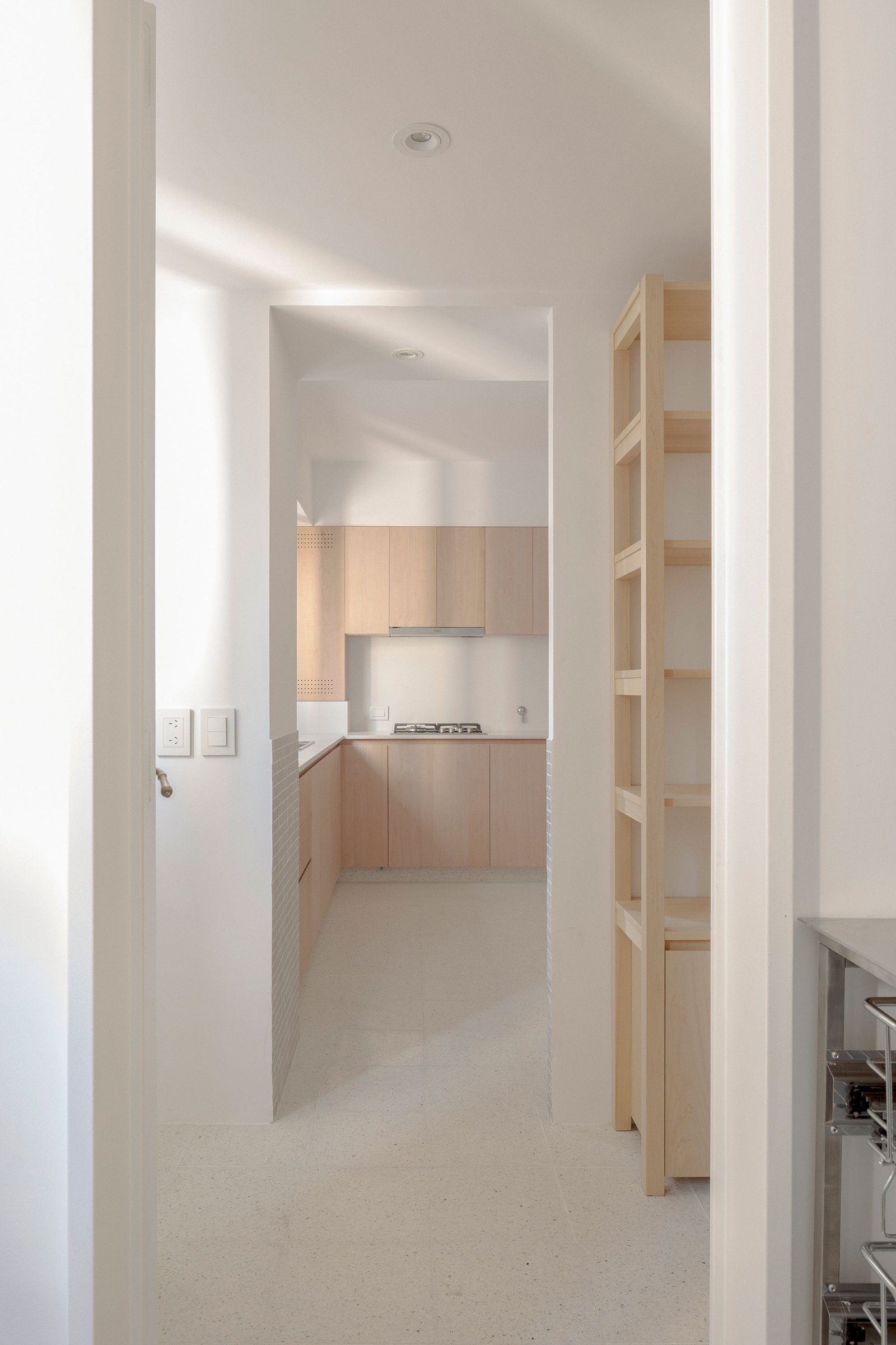 Cocina minimalista con gabinetes de madera clara y suelo de microcemento blanco — proyecto Reforma O'Higgins, por Estudio YME, en Belgrano
