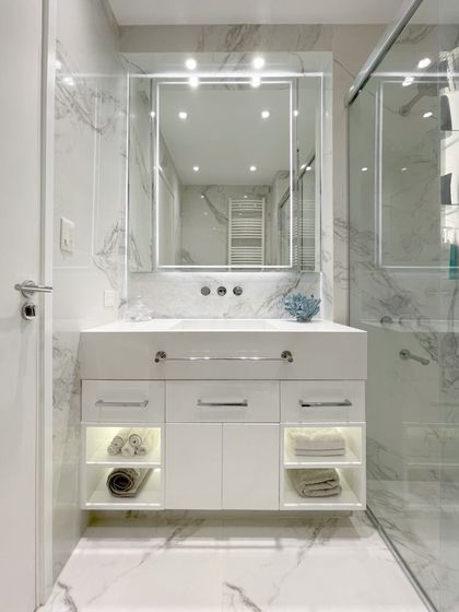 Baño minimalista con vanitory blanco, espejo iluminado y mármol — proyecto Remodelación Baño, por Estudio Nicolás Pierry
