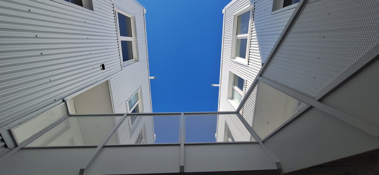 Fachada moderna con revestimiento de metal corrugado blanco y cielo azul — proyecto Edificio Escribano, por LW Lopez Wolder arquitectos, en Pasaje Escribano 66