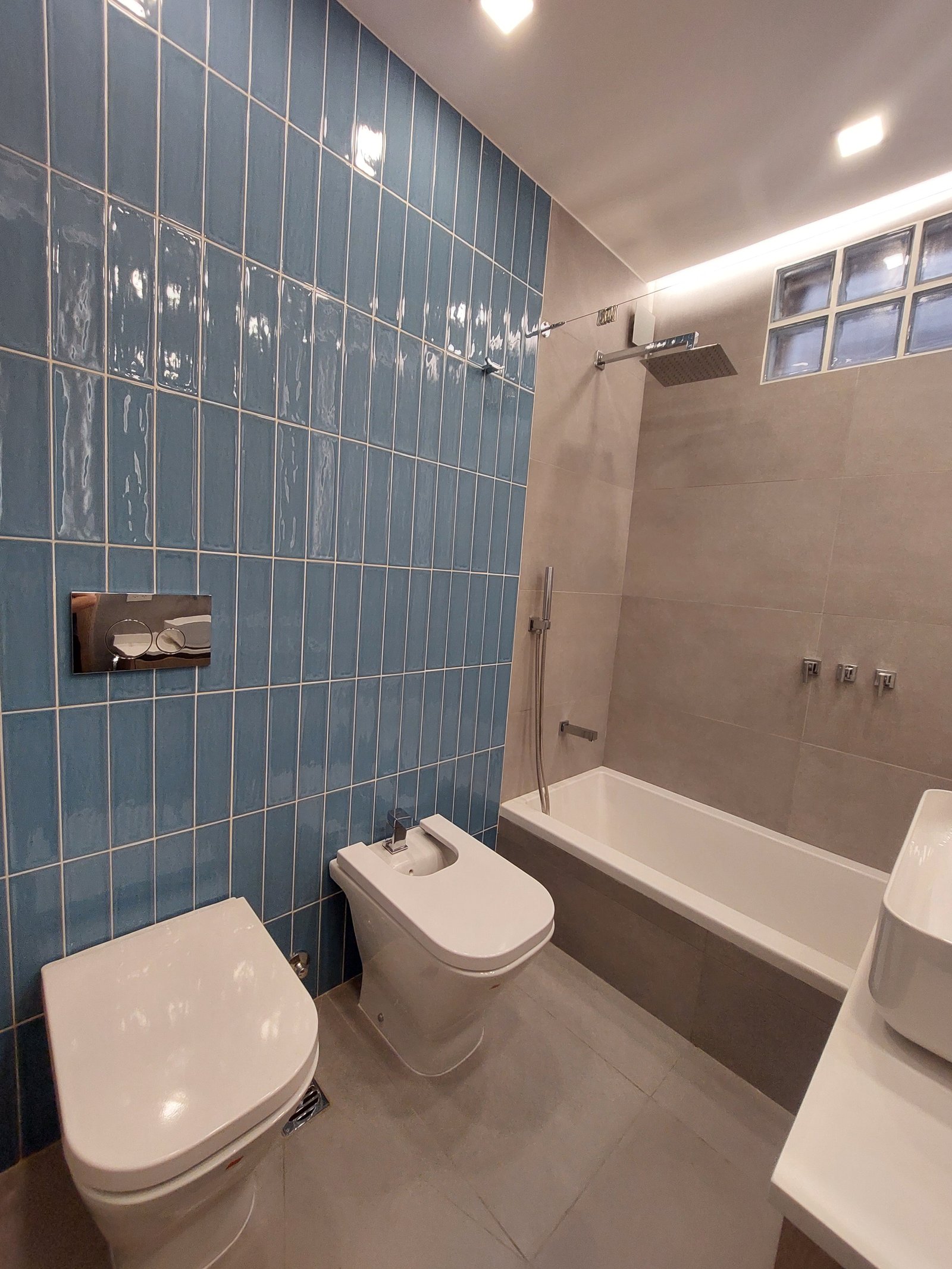 Baño moderno con azulejos azules verticales y sanitarios flotantes — proyecto FLORES, por Arquitecta, en Flores