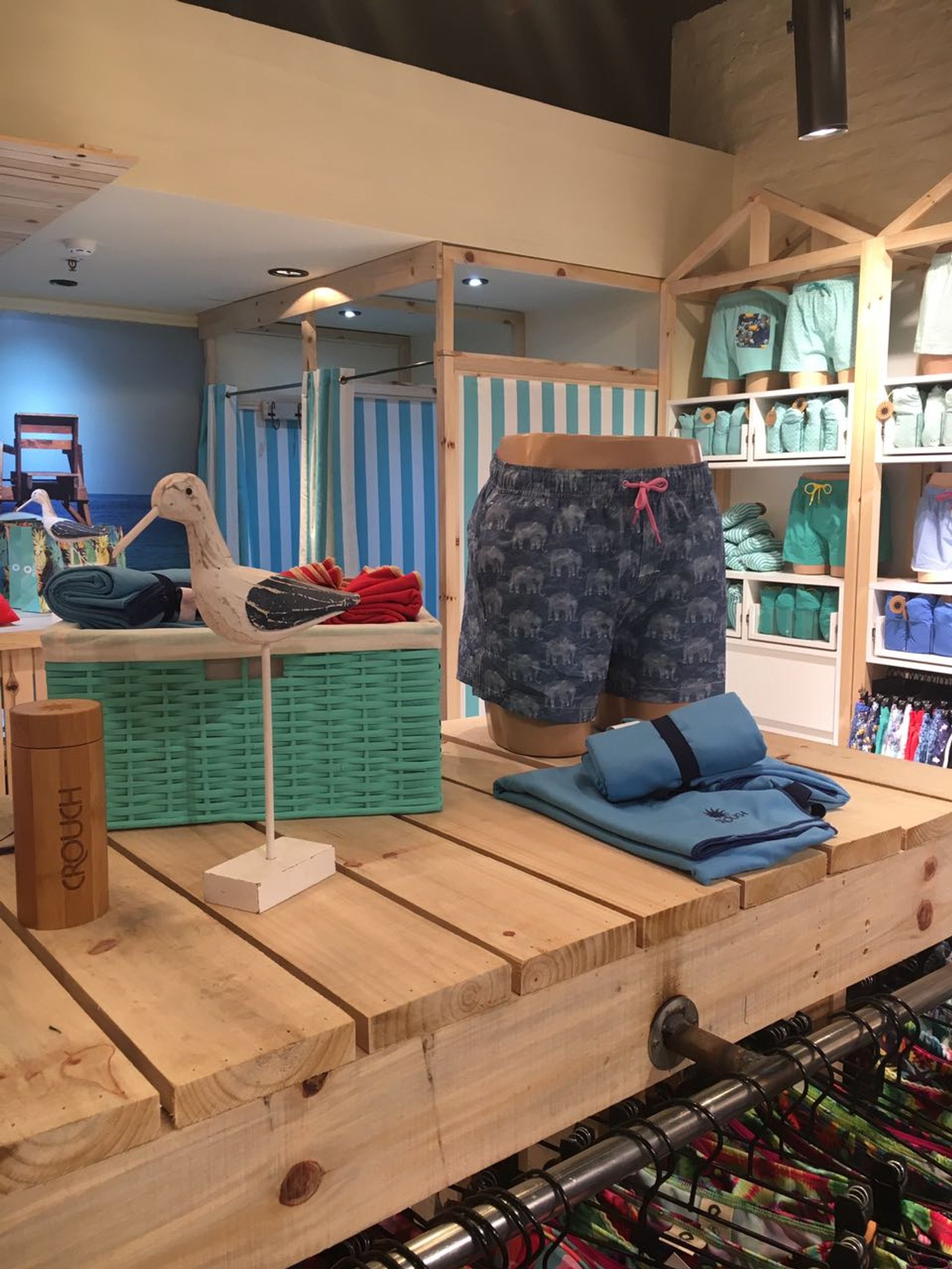 Loja de roupas de praia com prateleiras de madeira e cortinas listradas — projeto CROUCH, por DE DIOS Estudio, em Blvd. Juan Manuel de Rosas 658