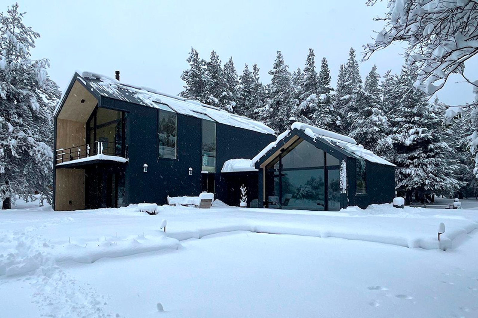 Casa moderna em floresta nevada com fachada escura e janelas amplas — projeto Vivienda Chihuallanca, por MUCHTEK, em San Martín de los Andes