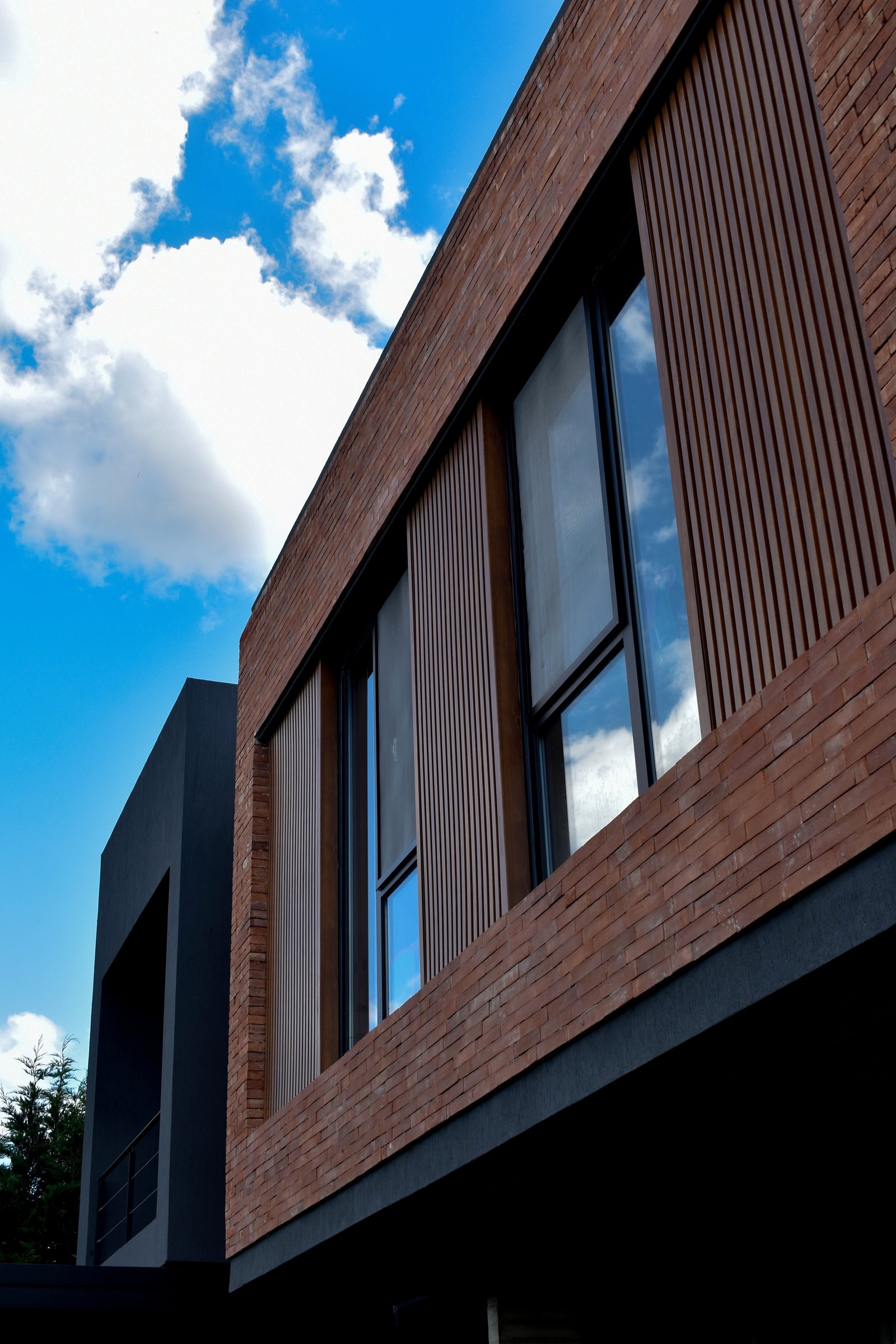Fachada moderna con ladrillo, madera y grandes ventanales negros — proyecto CASA HC, por Daniel Daniele - Oficina de Arquitectura, en Canning