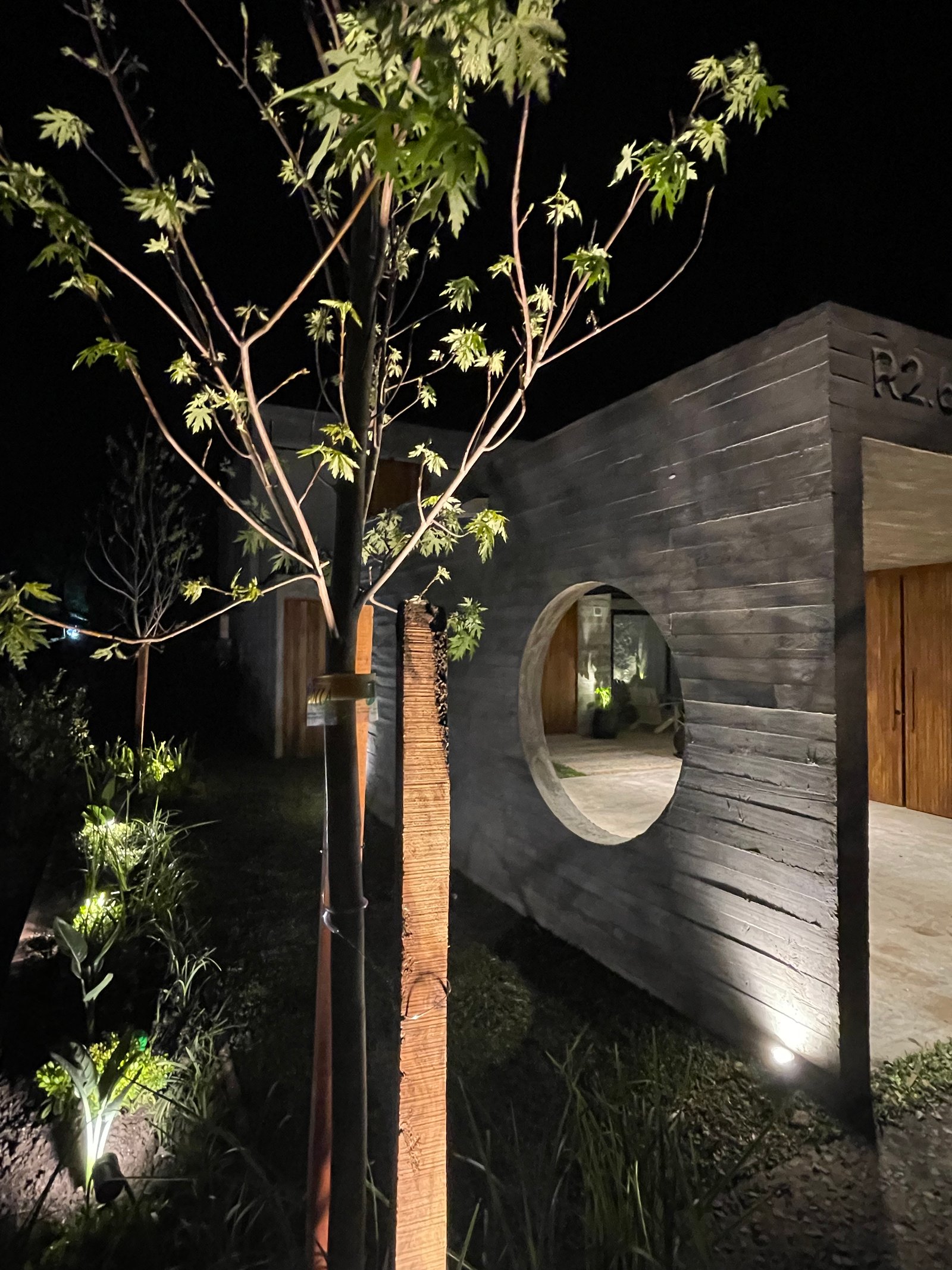 Fachada moderna de hormigón con arco circular y vegetación iluminada — proyecto COSTA ESMERALDA, por Baires Green, en Pinamar