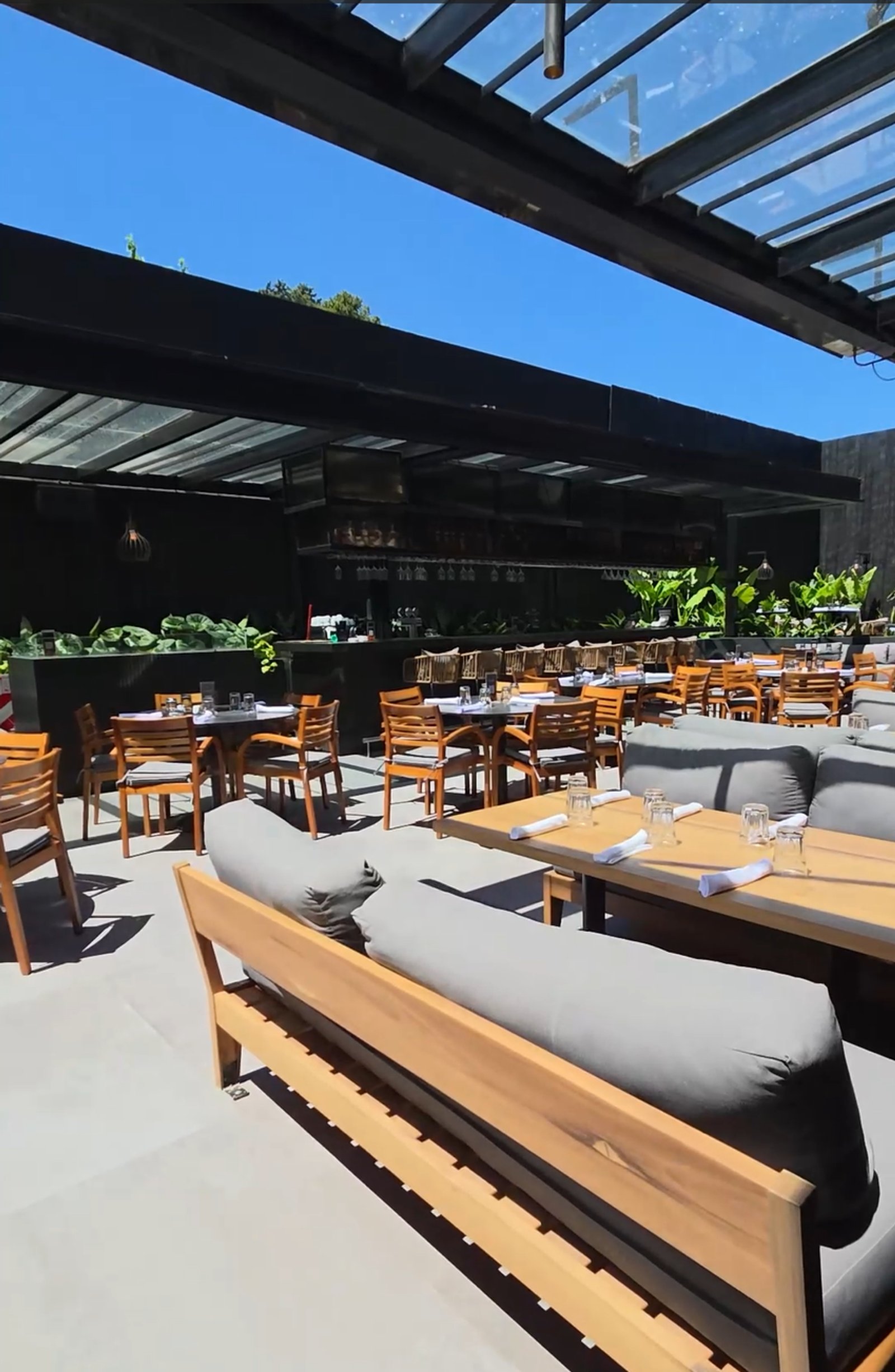 Terraza moderna con sofás de madera y techo de cristal — proyecto GRILLER - Restaurante, por GALPON OSUNA, en Canning